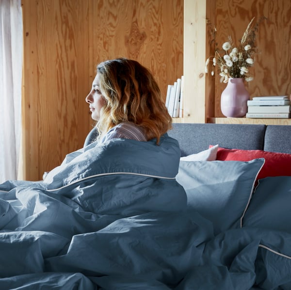 一位女性坐在床上望向窗外,身上裹着蓝色白边的kungsblomma 昆布鲁玛