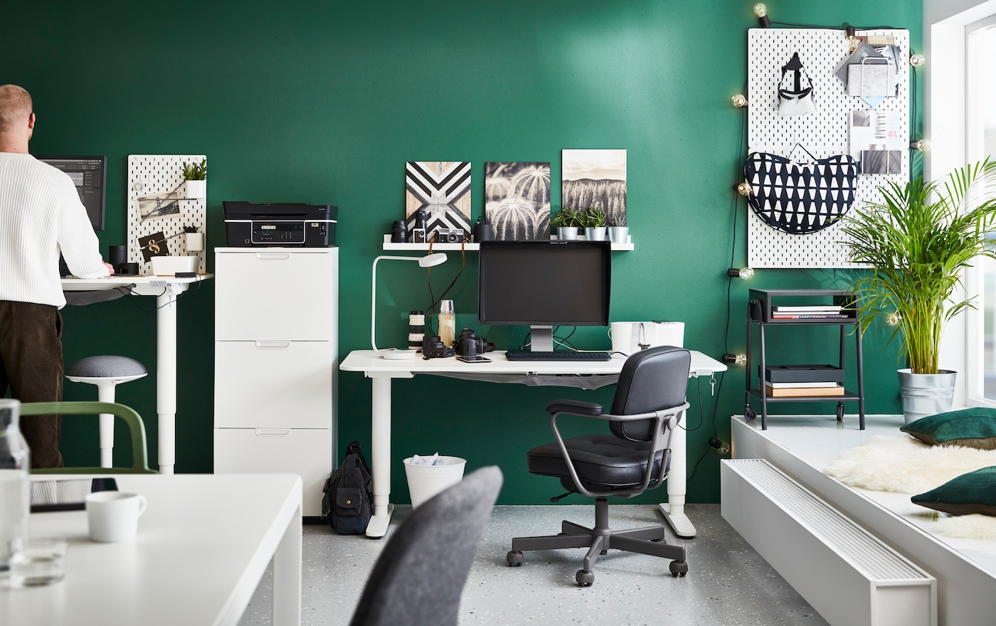 BEKANT white sit-stand desks in a green-walled office space with aALEFJÄLL black swivel chairs and NILSERIK stool.