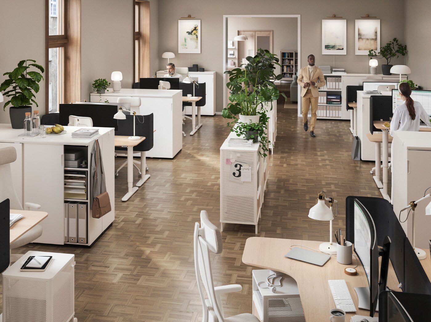 An open plan office with a central shelving unit decorated with plants, and workstations with lighting around the edge.