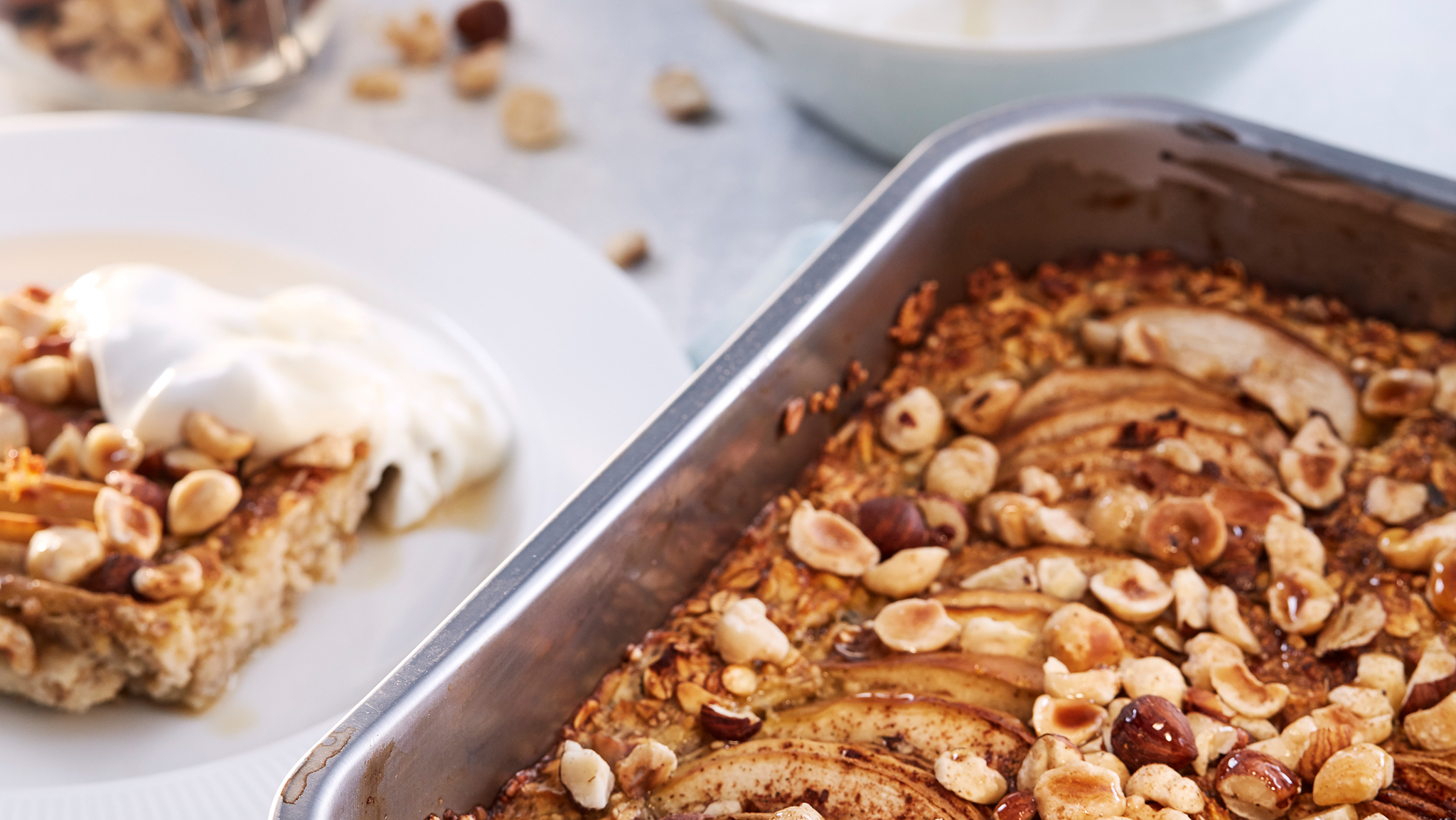 A baking tin containing cooked HJÄLTEROLL porridge by a white plate with a slice of porridge and a dollop of yoghurt on it.