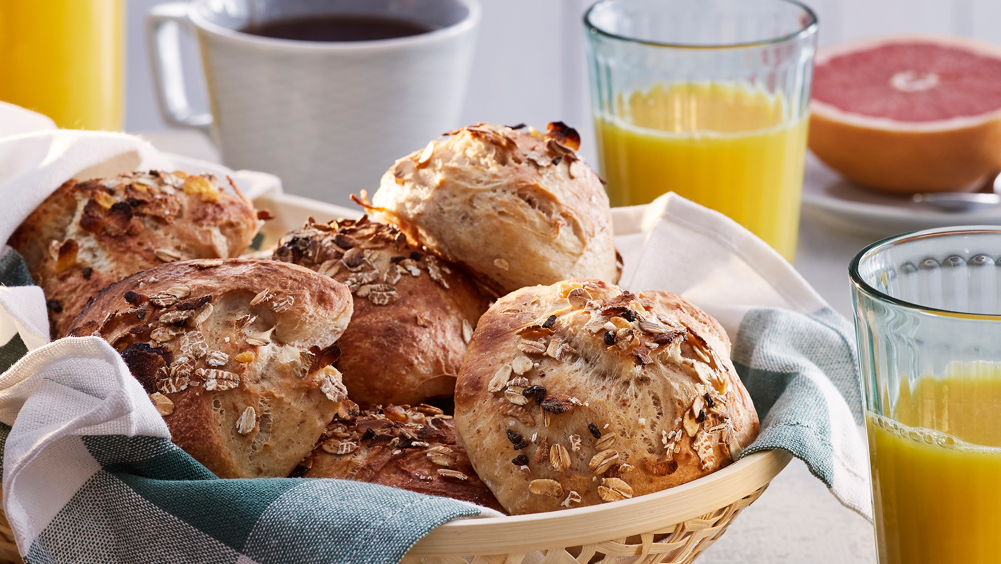 A basket of rolls made with HJÄLTEROLL muesli on a breakfast table by a cup of coffee, orange juice and half a grapefruit.