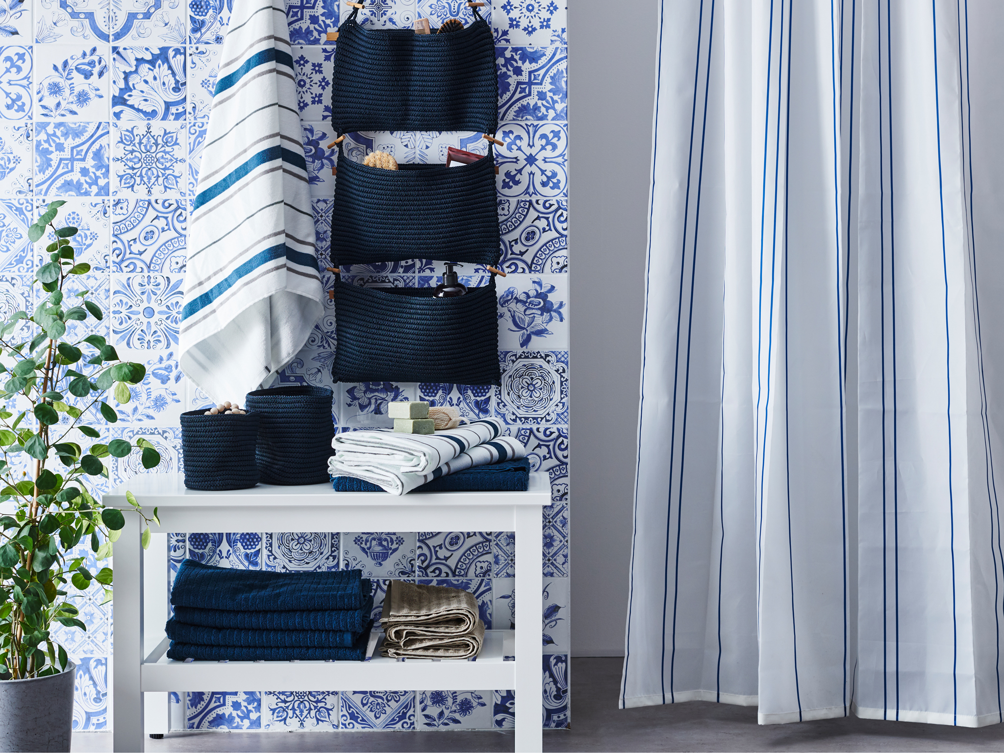 A bathroom with a white HEMNES bench, some towels, some blue baskets and hanging storage plus a shower curtain.