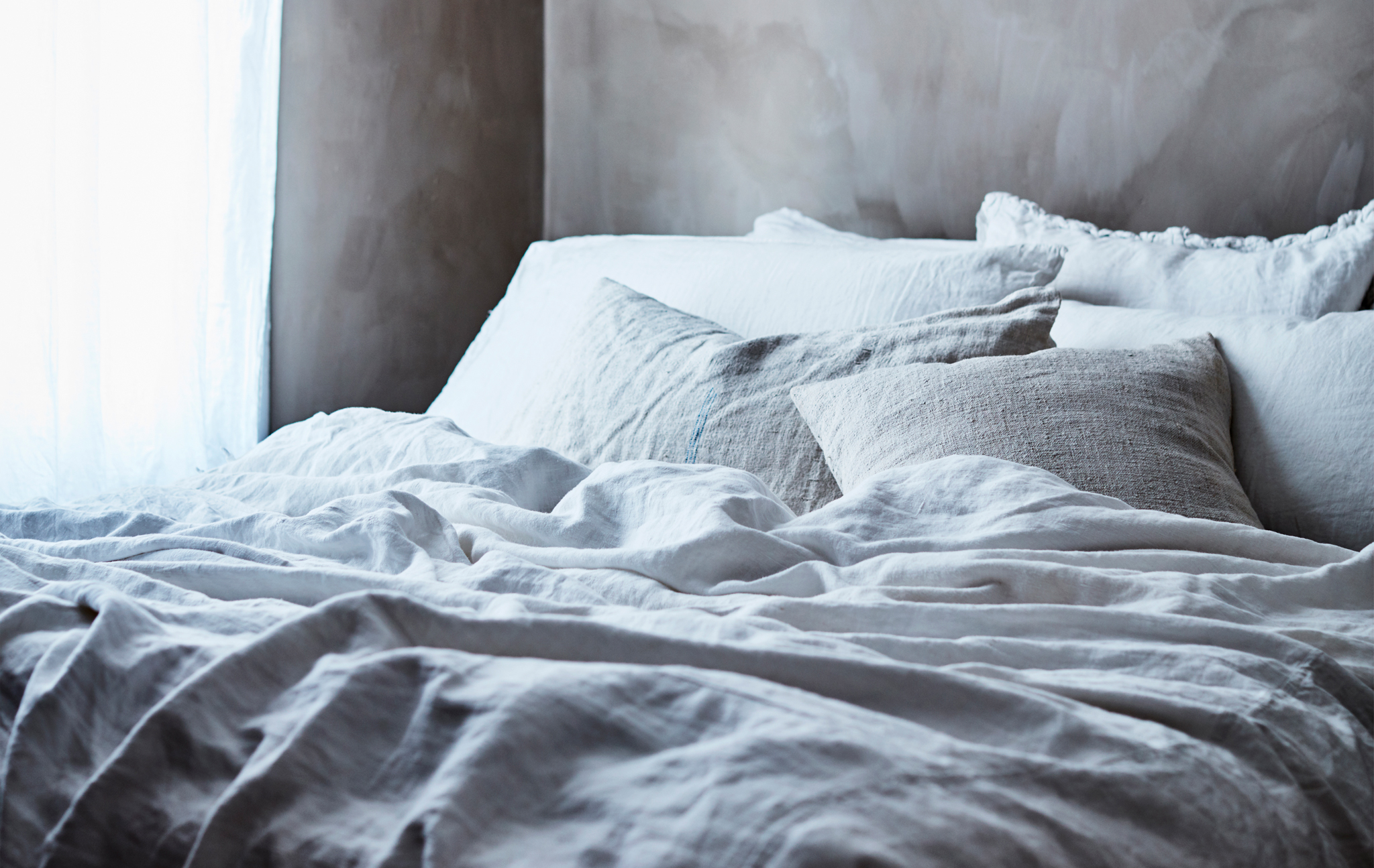 A bed dressed with layers of grey and white bedding.