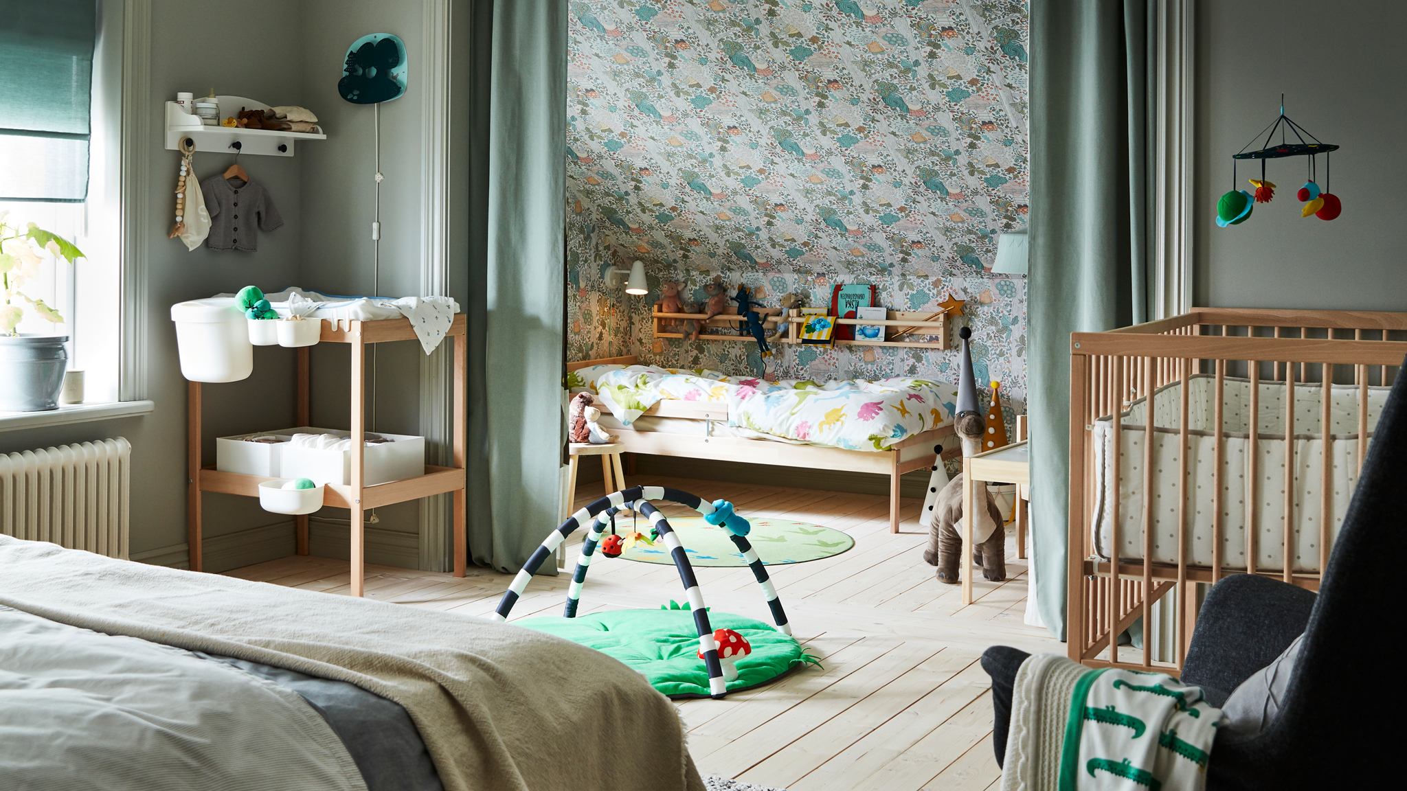A bedroom containing a double bed, SNIGLAR cot, changing table and child’s bed with rail, and curtains dividing the space.