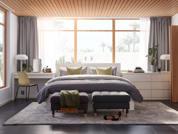 A bedroom with a dressing table, a bed frame and a chest of drawers from the MALM series and a large grey rug on the floor.