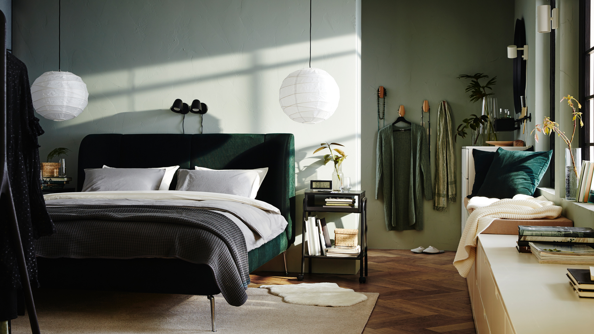 A bedroom with a green TUFJORD bed and two SKURUP lamps on the wall behind it. NORDLI drawer units run along the side wall.