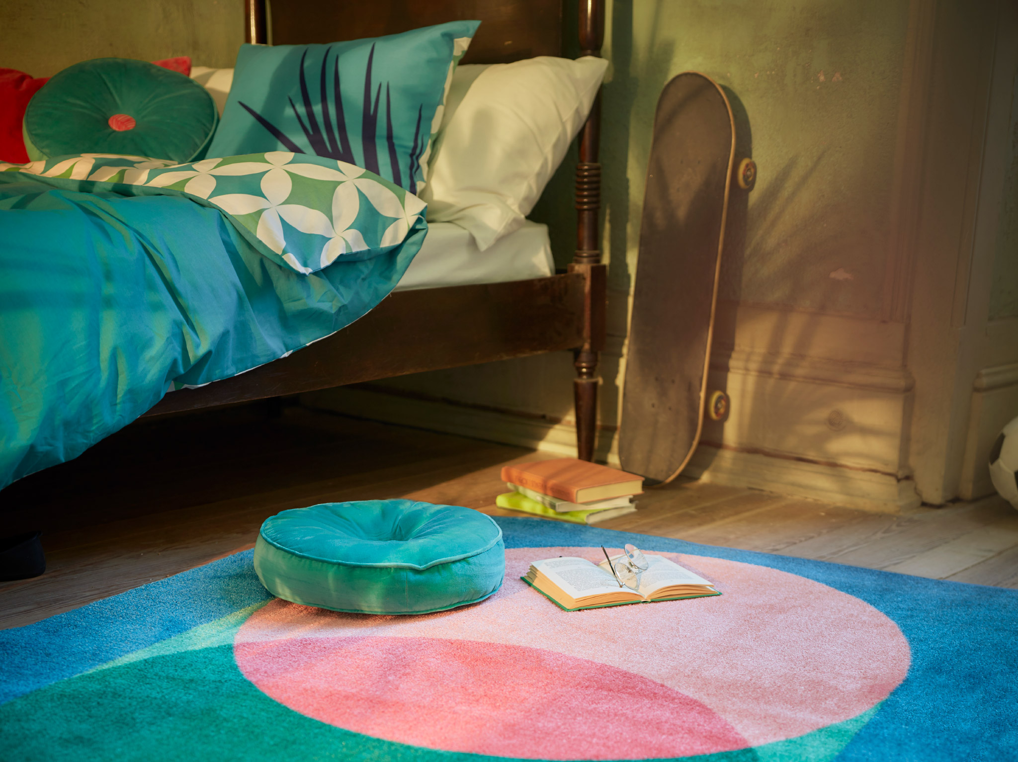 A bedroom with GRACIÖS textile series in turquoise tones including a quilt cover, patterned rug and a round velvet cushion.