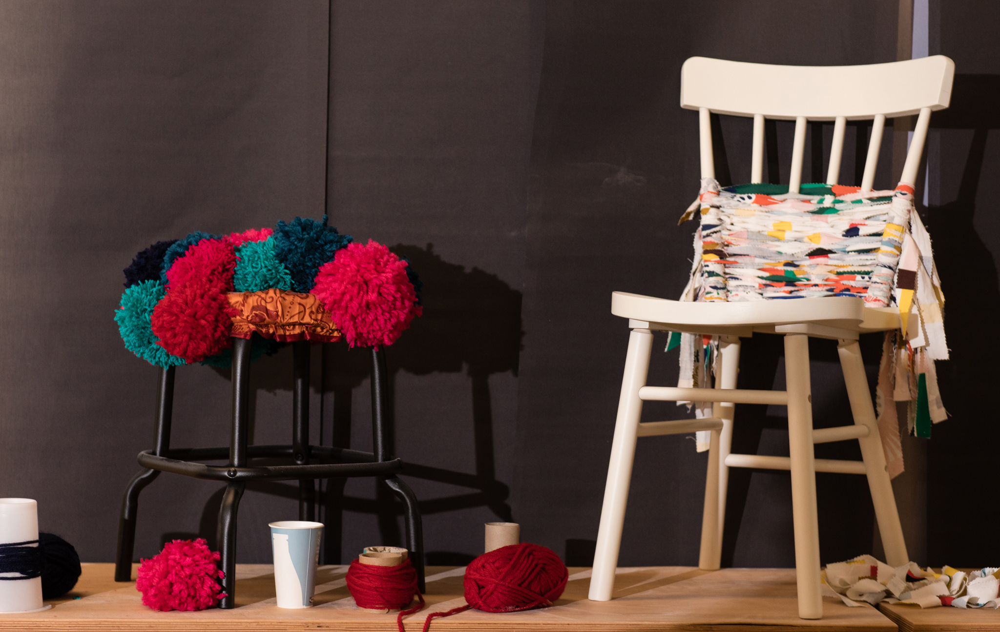 A black stool decorated with knitted shapes and a white chair decorated with scraps of fabric.