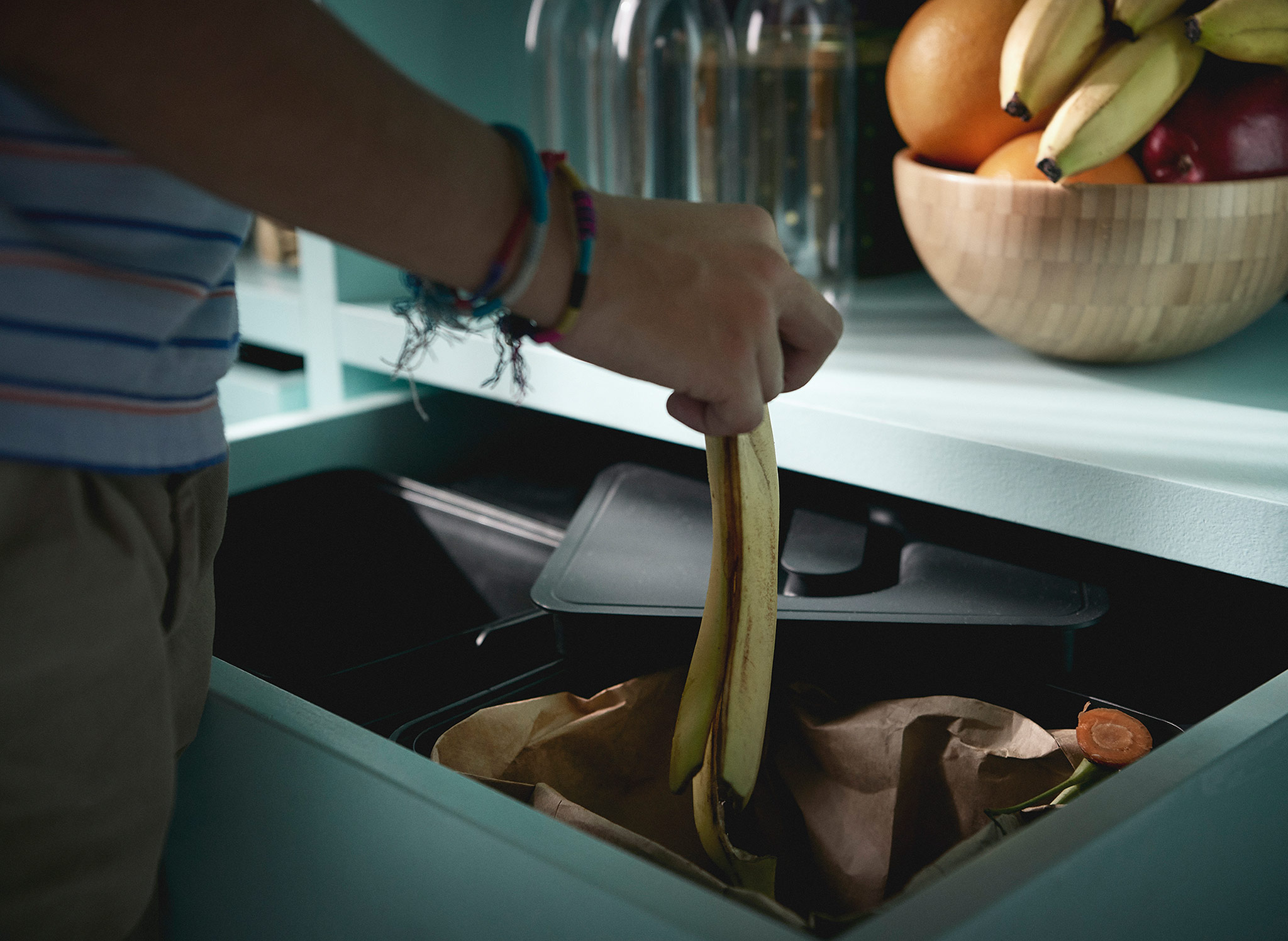 A boy wearing bracelets recycling a banana peel in the VARIERA recycling system.