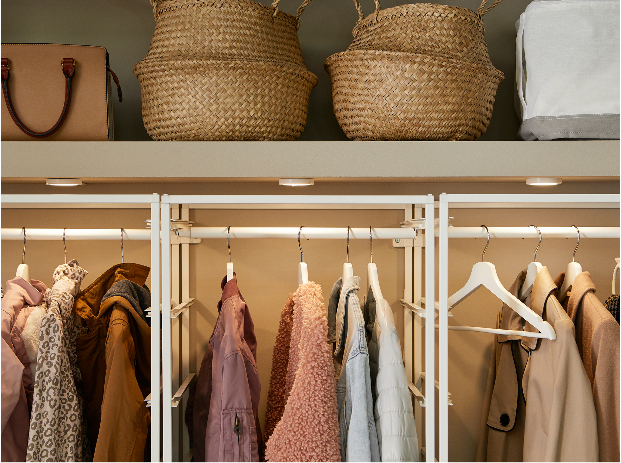A built-in closet with JONAXEL white storage system inside with clothes rails, lighting and baskets in seagrass.