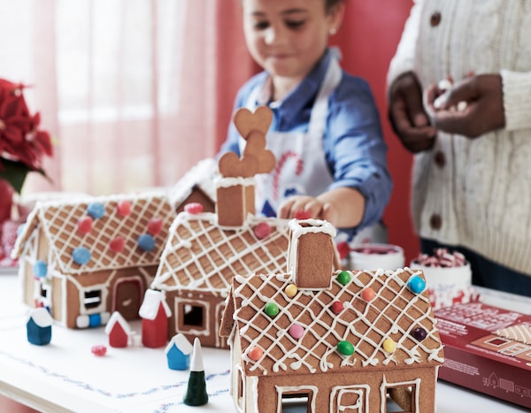 A child building three VINTERSAGA model houses made of baked gingerbread dough and decorated with icing and sweets.