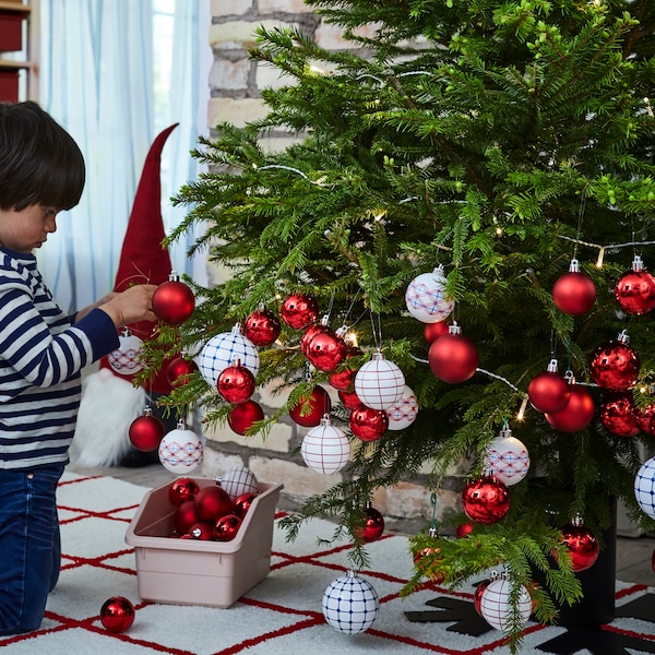 A child decorating a Christmas tree with a mix of red and white patterned VINTERFEST deco baubles.