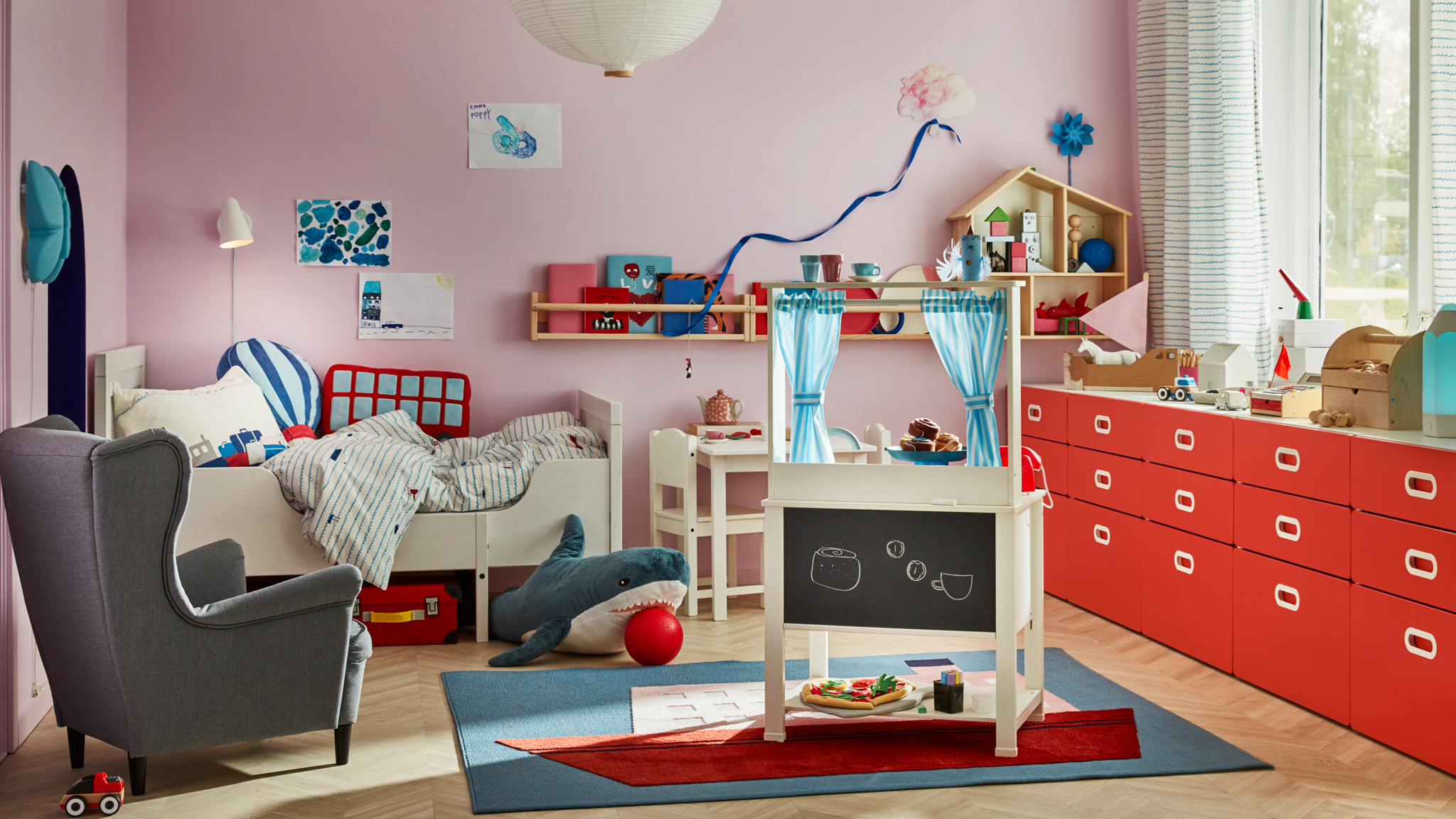 A children’s room with a SPISIG play kitchen with curtains, a STRANDMON children’s armchair and a SUNDVIK extendable bed.
