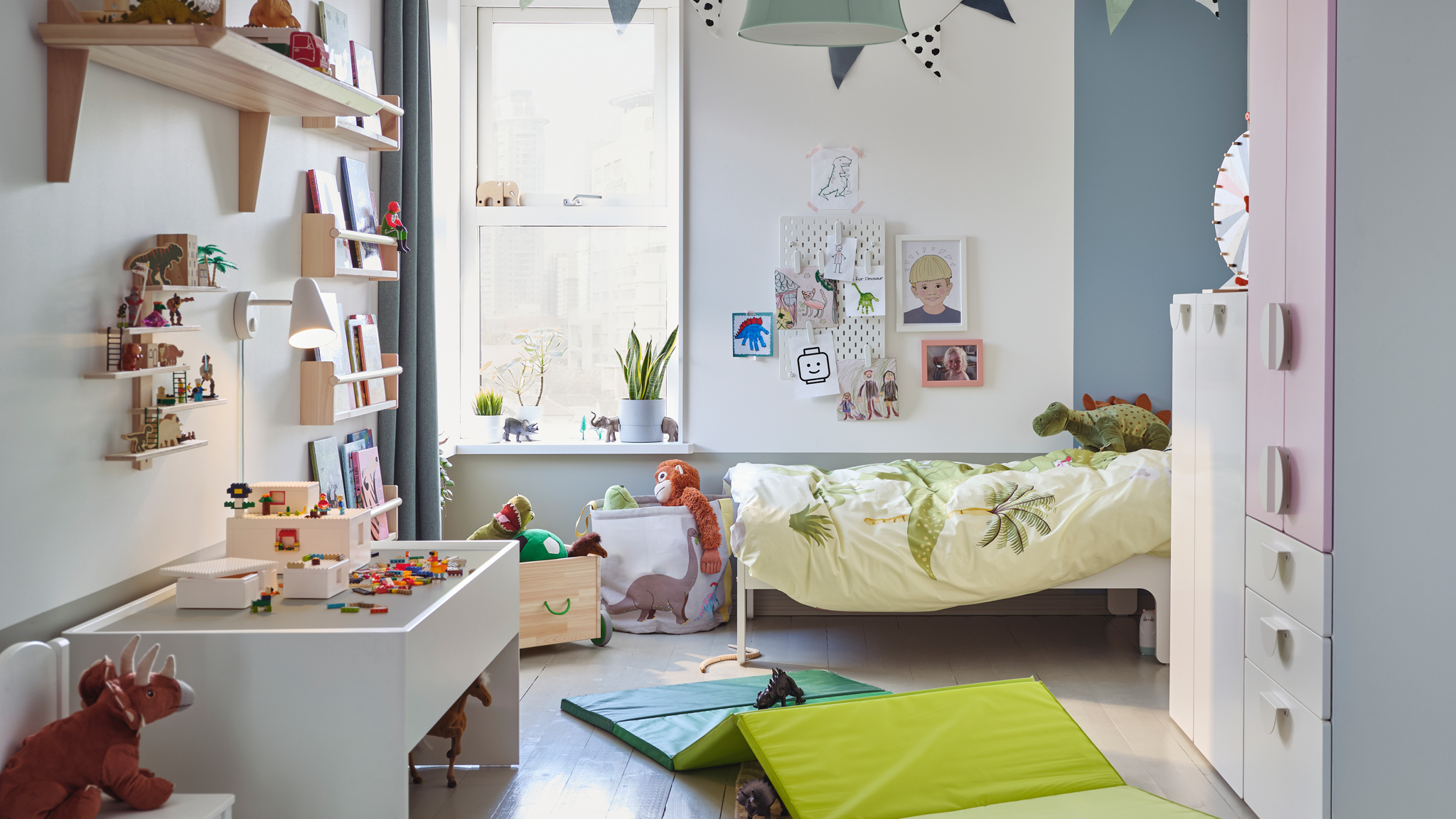 A child’s bedroom with a SLÄKT extendable bed in the corner and SMÅSTAD storage opposite a DUNDRA activity table.