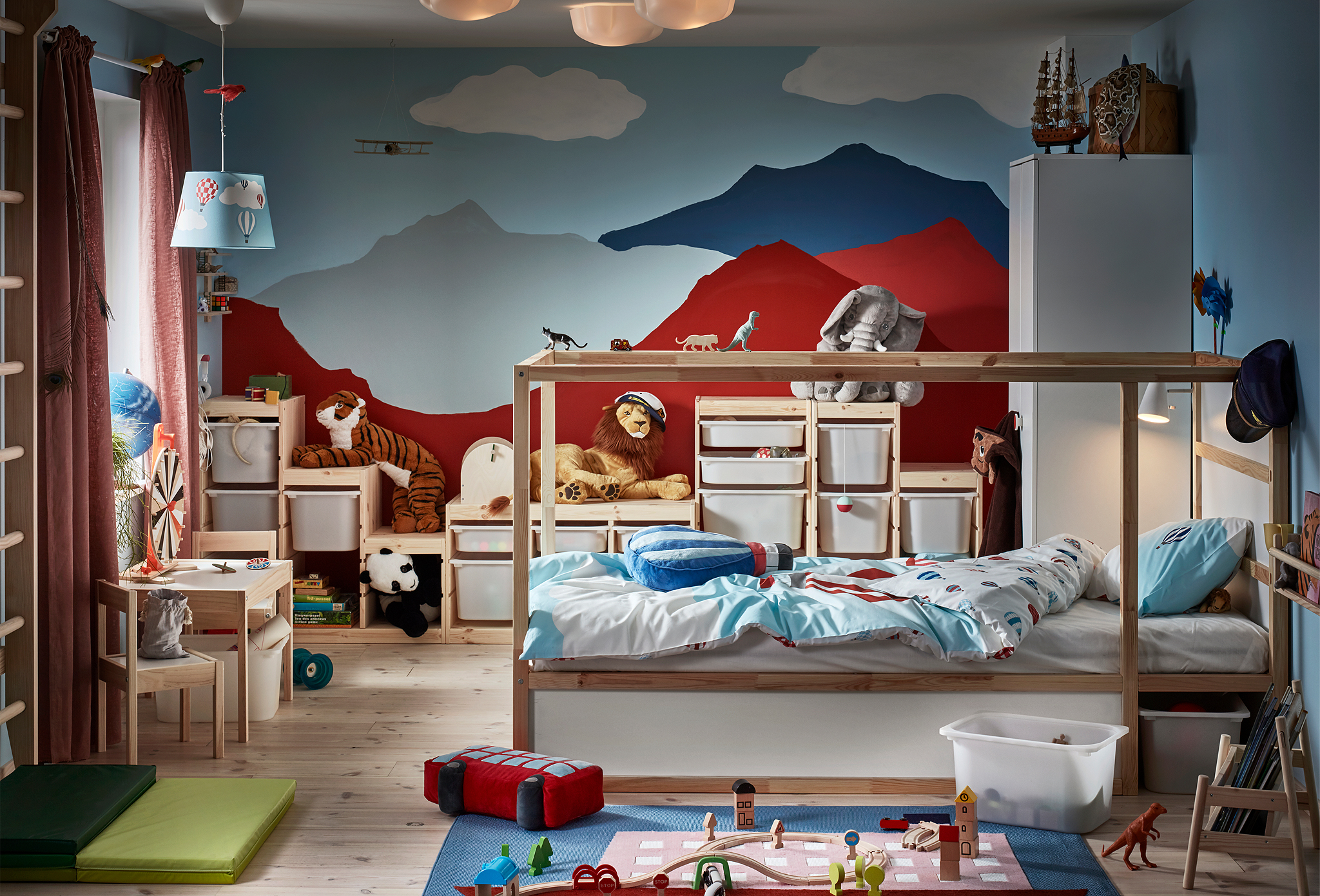 A child’s room visually dominated by a back wall with painted mountains. Reversible bed, wall bars, toys, various storage.