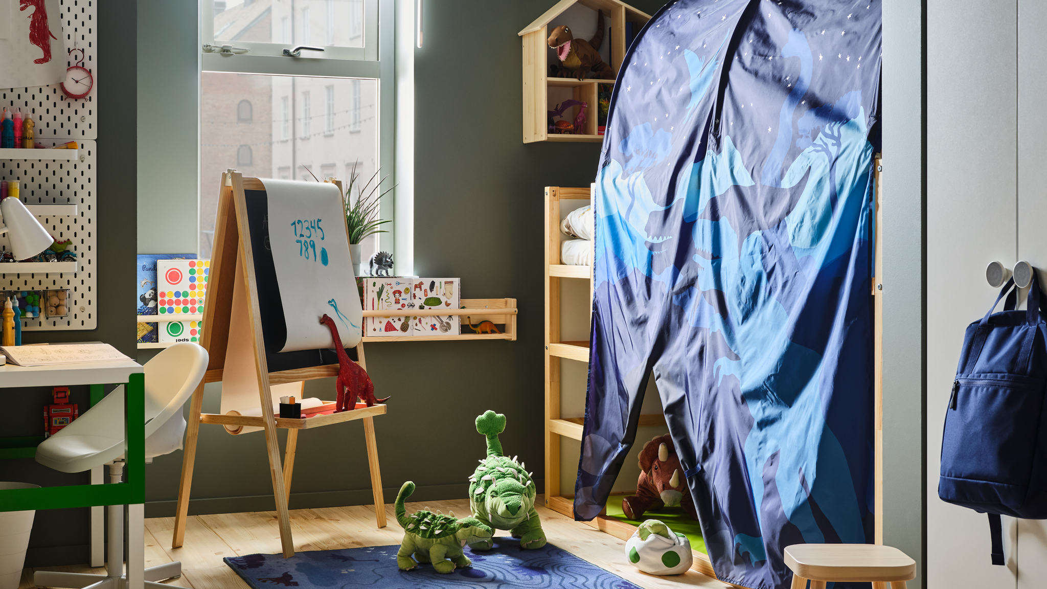 A child’s room with a KURA reversible bed with a KURA bed tent and lots of toy dinosaurs. A MÅLA easel is near the bed.