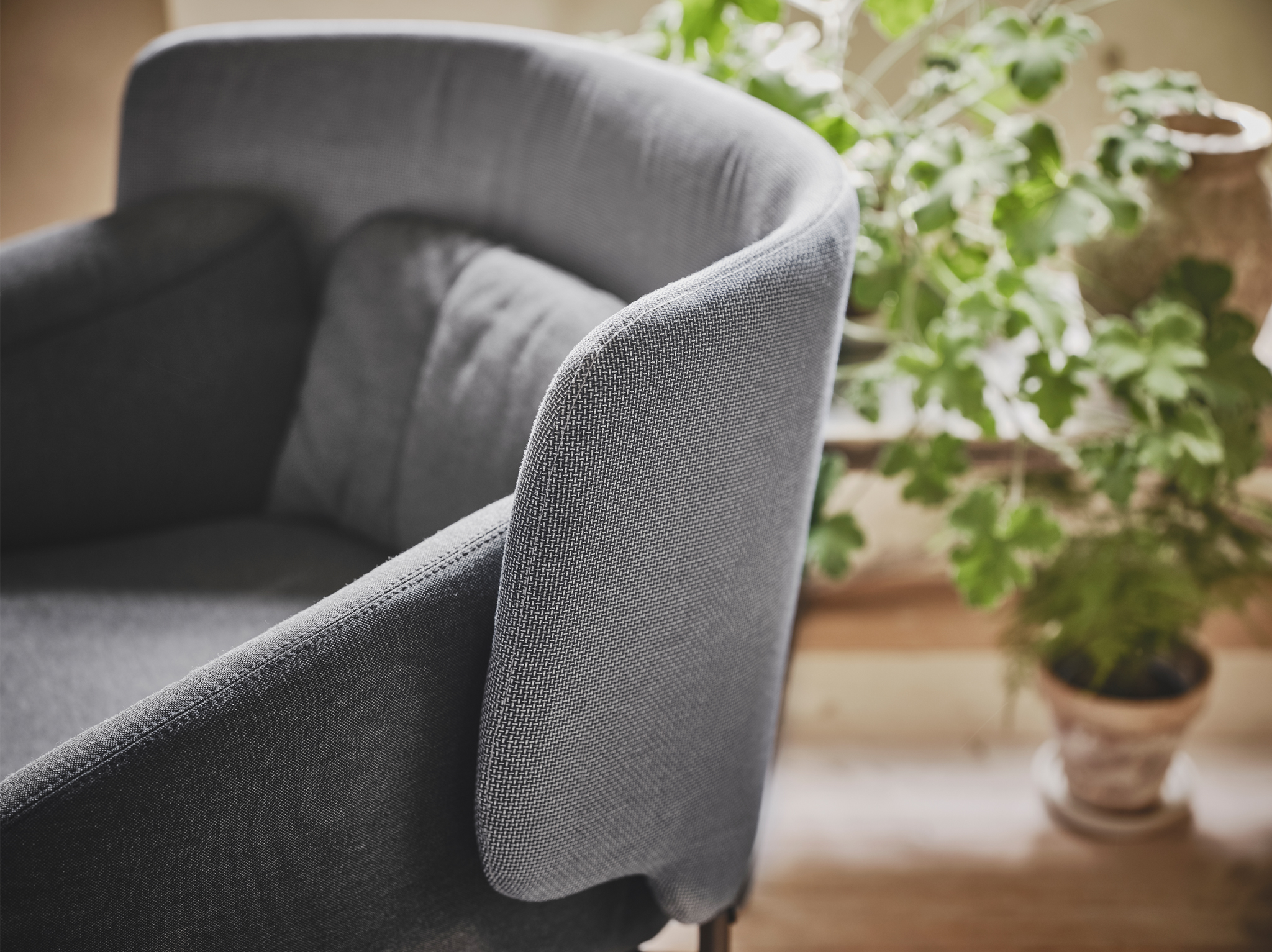 A close-up of a grey low back BINGSTA armchair featuring curved armrests and an enclosing back panel.