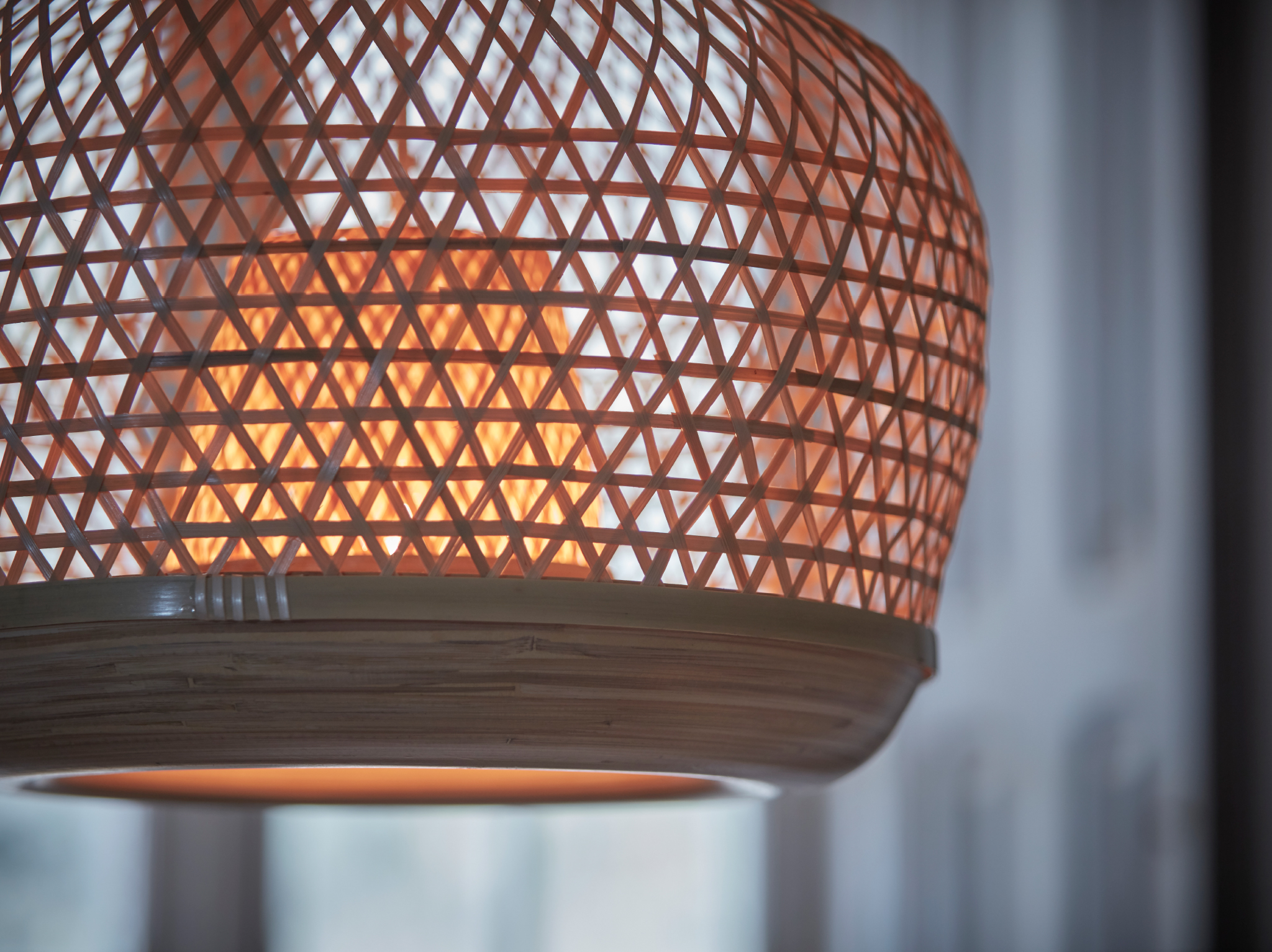 A close-up of a switched on MISTERHULT pendant lamp handwoven in the light, natural material bamboo.