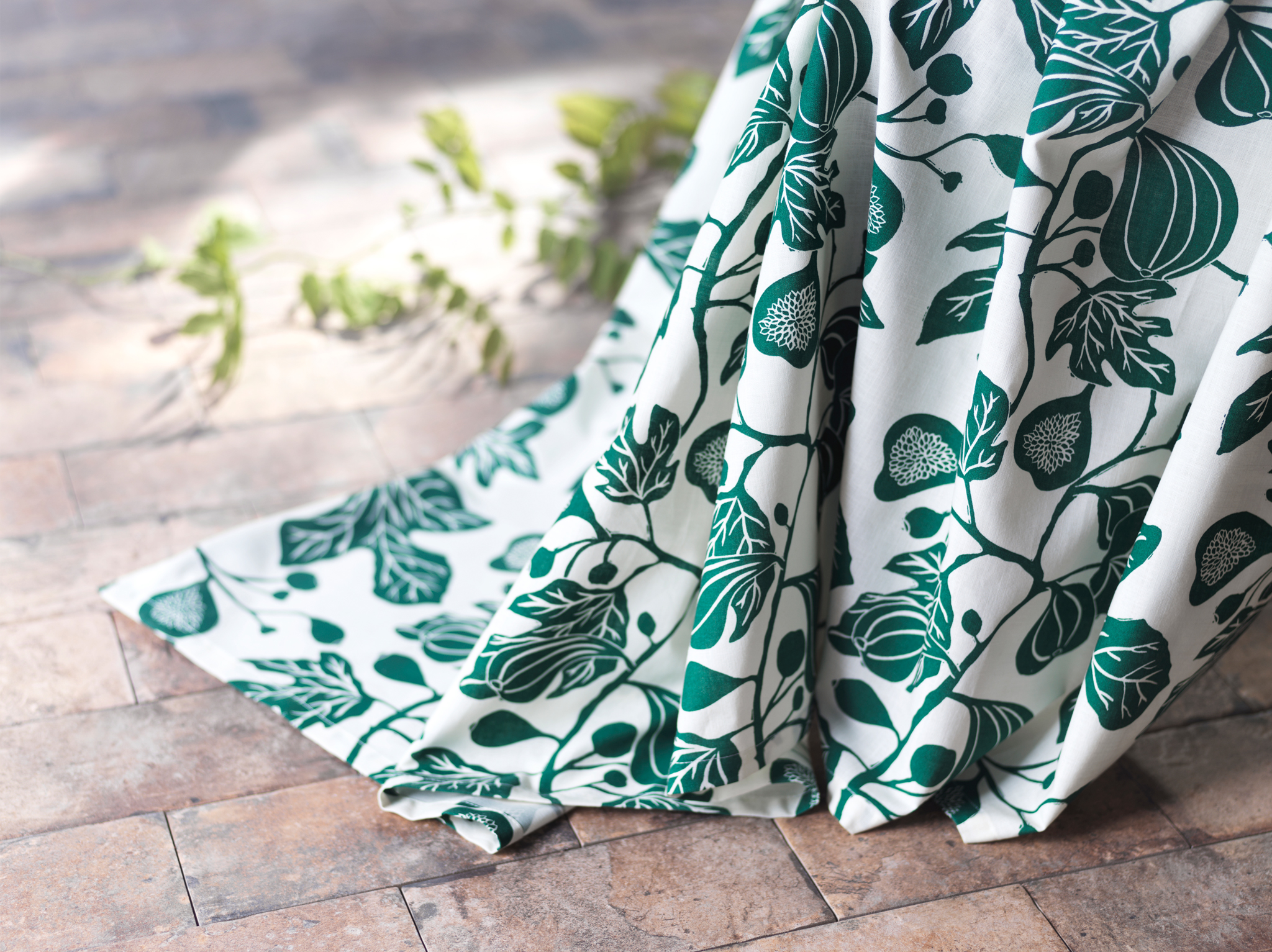 A close-up of ALPKLÖVER curtains featuring a winding pattern of fig leaves in white and green reaching to the floor.