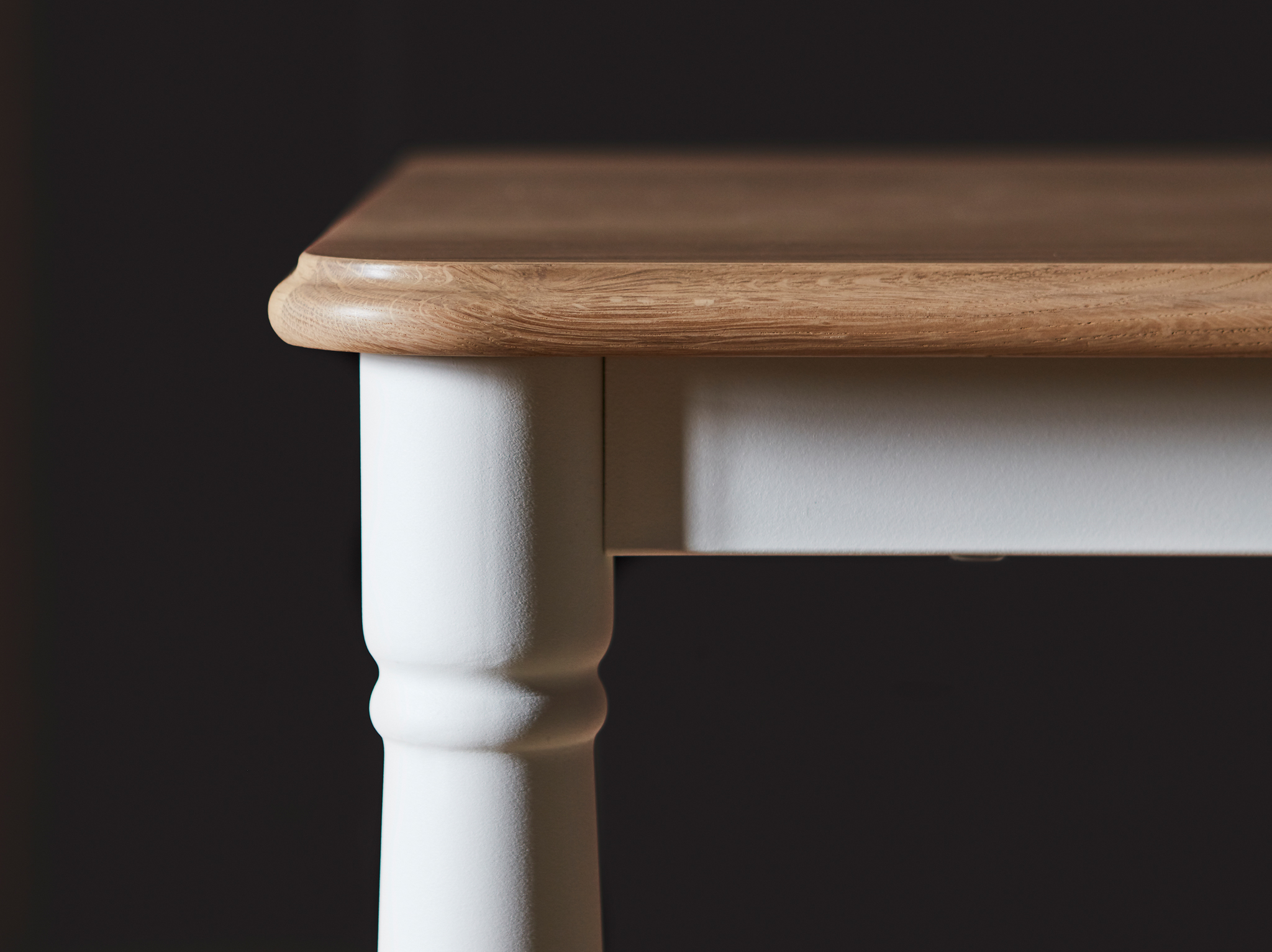 A close-up of DANDERYD dining table with an oak veneer table top and white legs shaped in a traditional style.