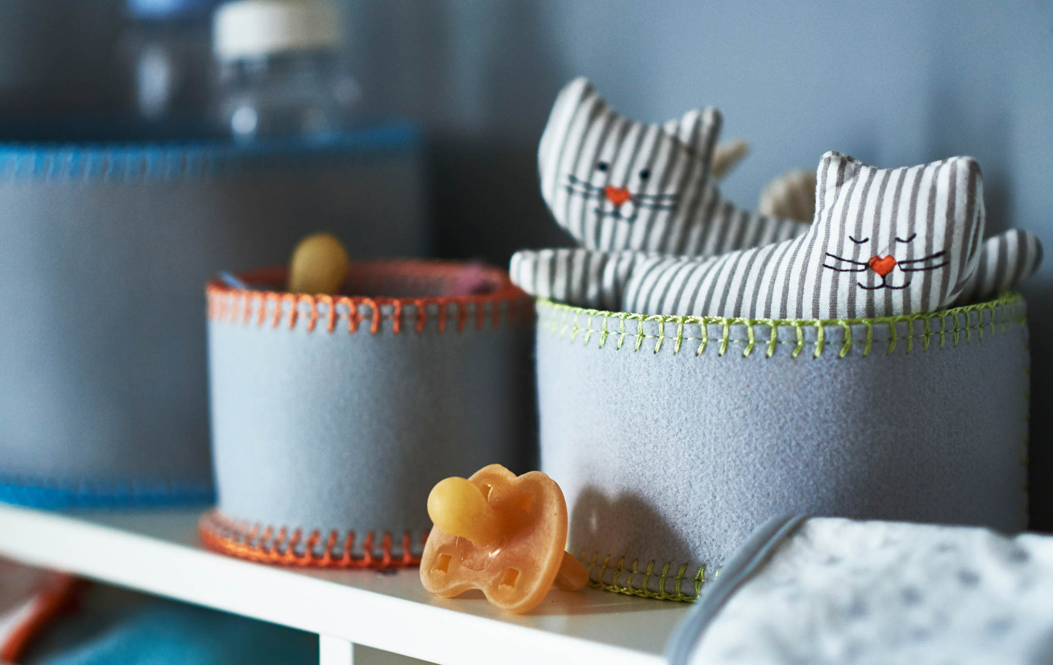 A close-up of felt storage baskets holding baby stuff like dummies and cat-shaped rattles