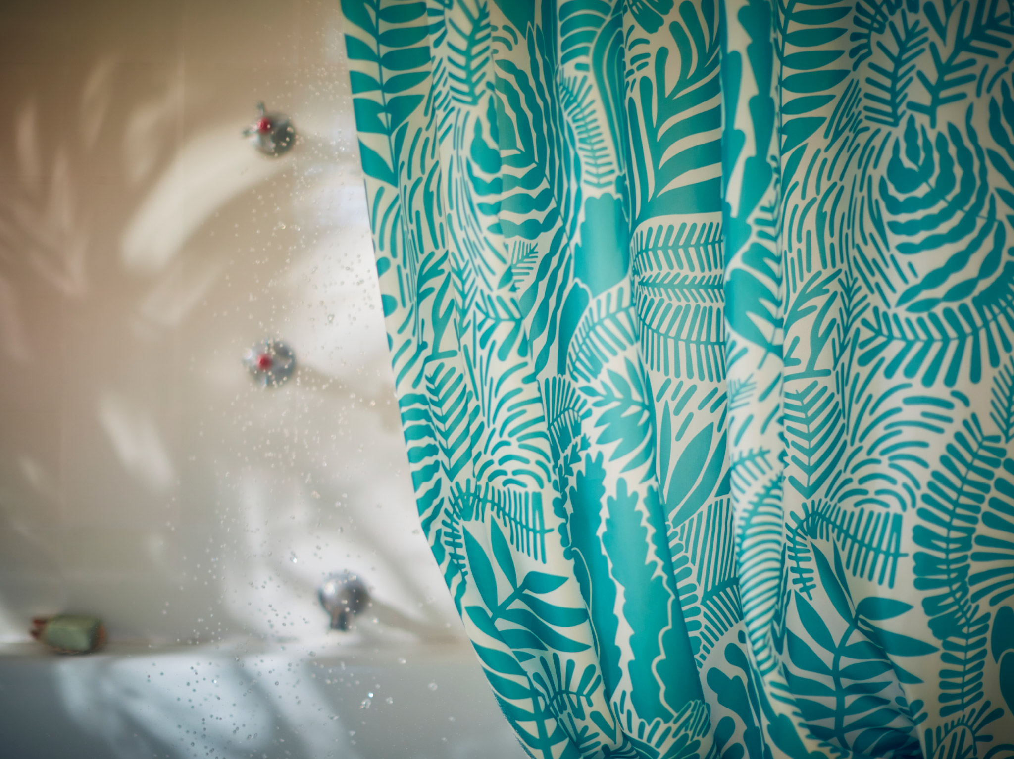 A close-up of GATKAMOMILL shower curtain with a leafy and playful pattern in turquoise and white in connection to a bathtub.