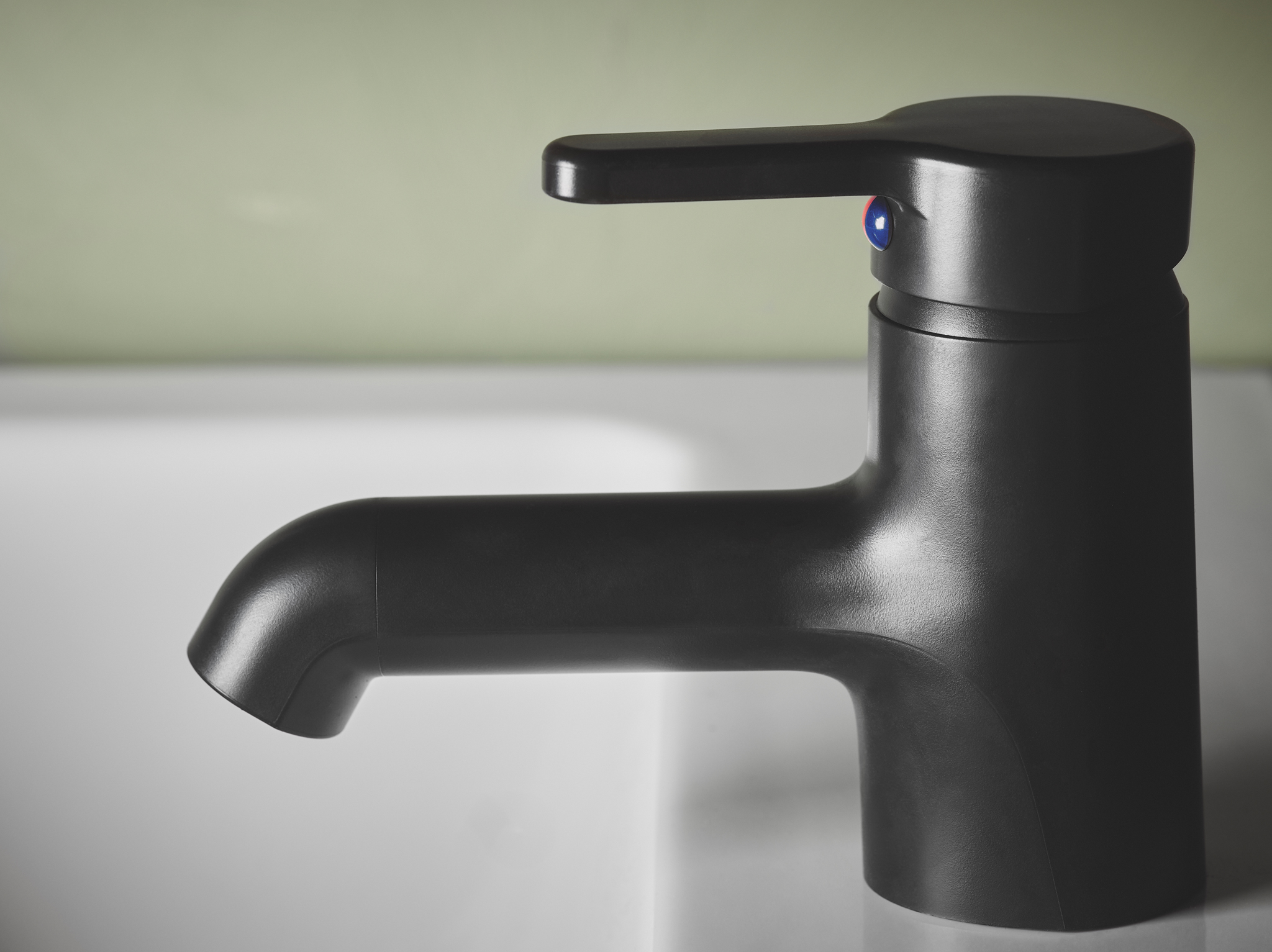 A close-up of SALJEN wash-basin mixer tap made in a sleek design of black plastic, used by a white wash-basin.