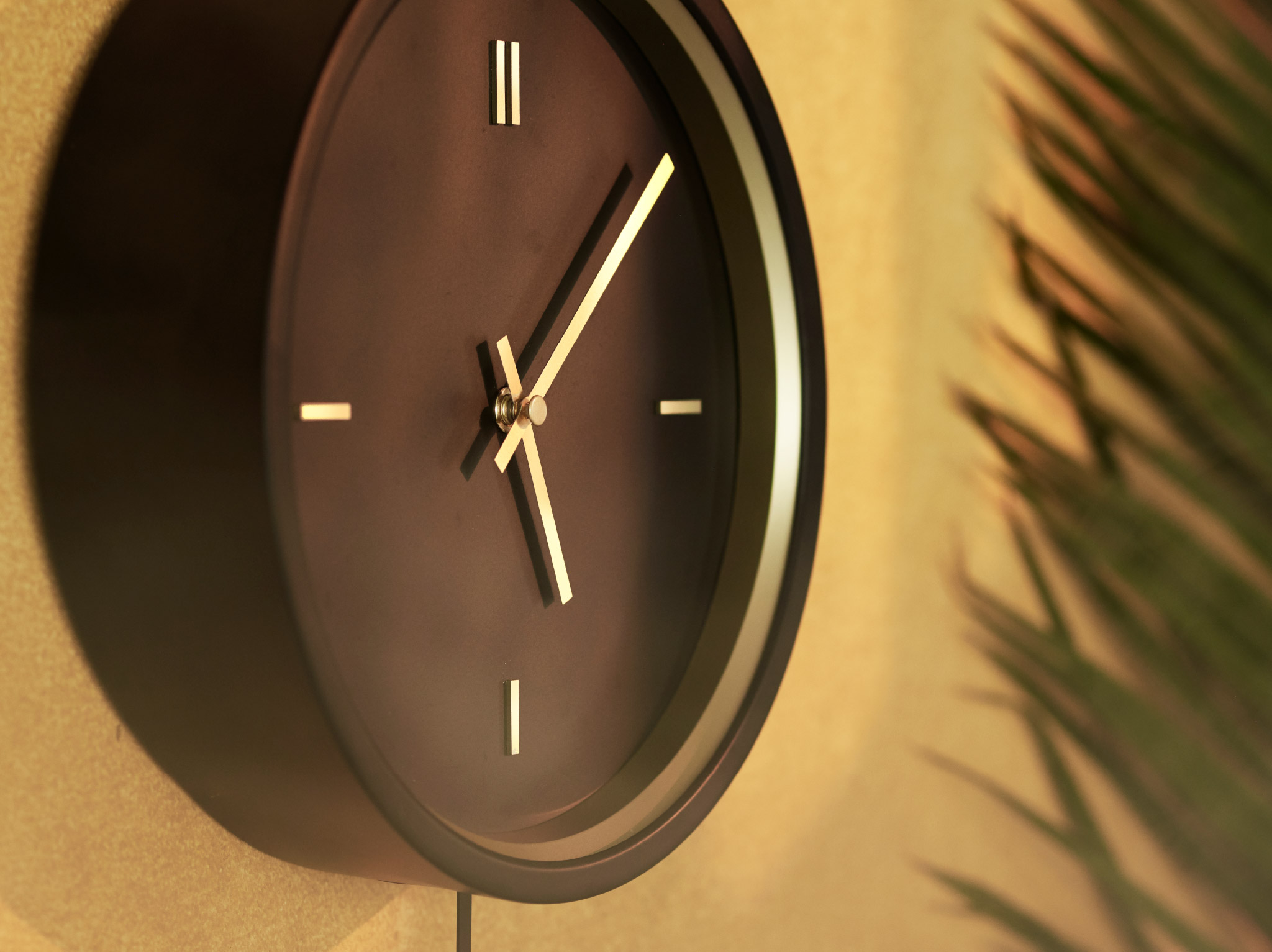 A close-up of the black STURSK wall clock with gold details and hands, hung up on a golden-brown wall.