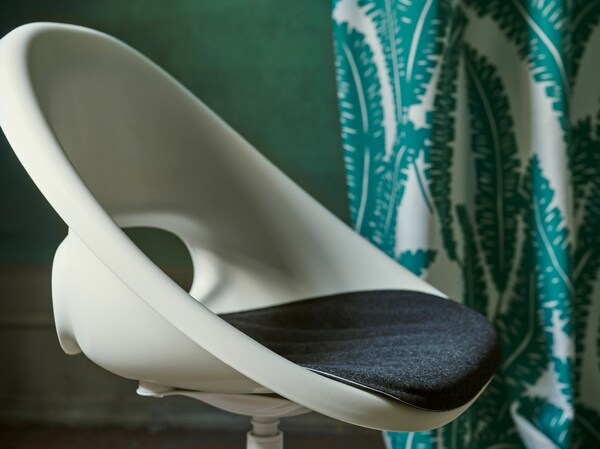 A close-up of the white LOBERGET/BLYSKÄR swivel chair with a rounded retro design placed in a green room.