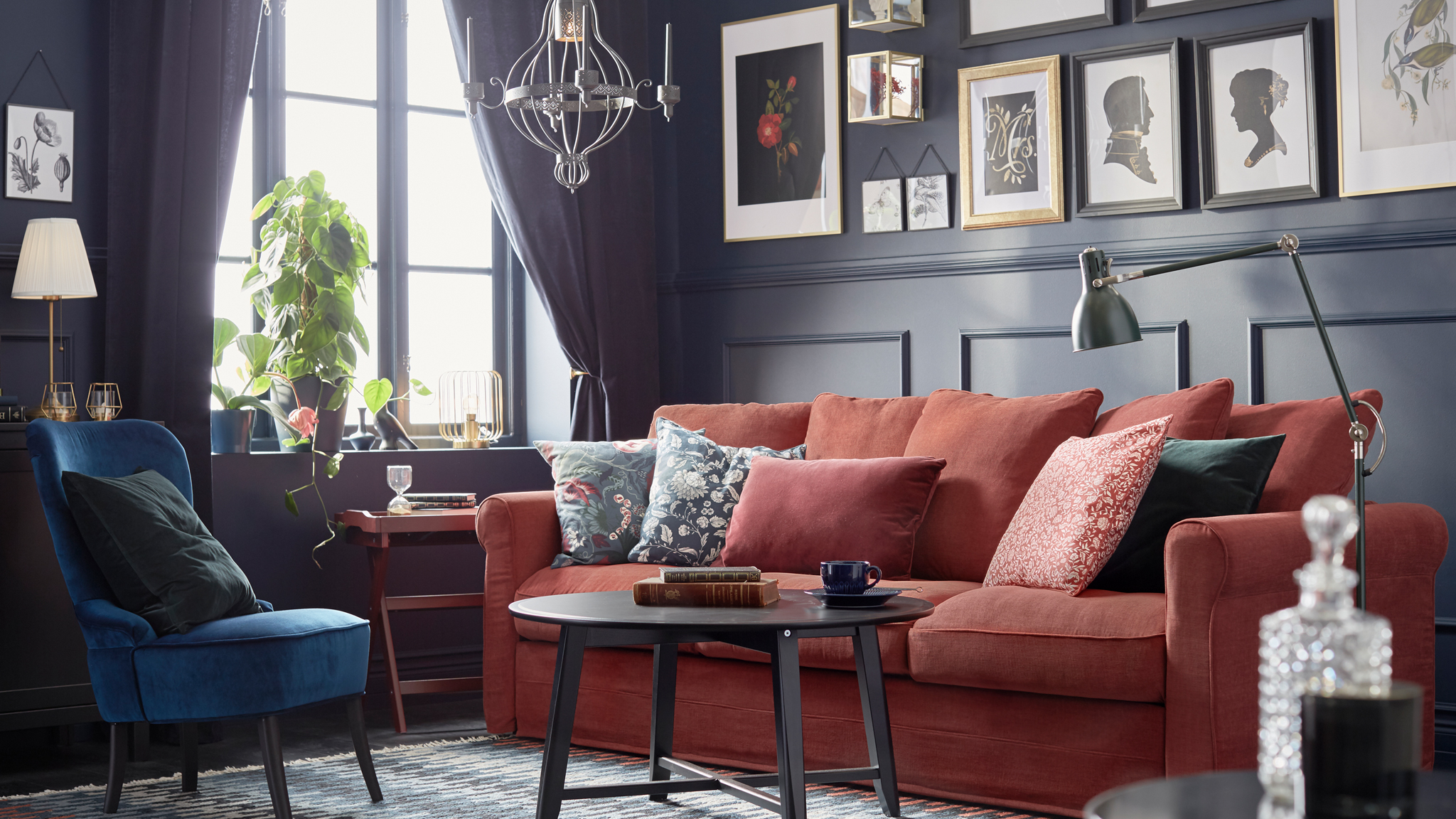 A dark-panelled, traditionally styled room with framed art, a red GRÖNLID sofa with cushions and a KRAGSTA coffee table.