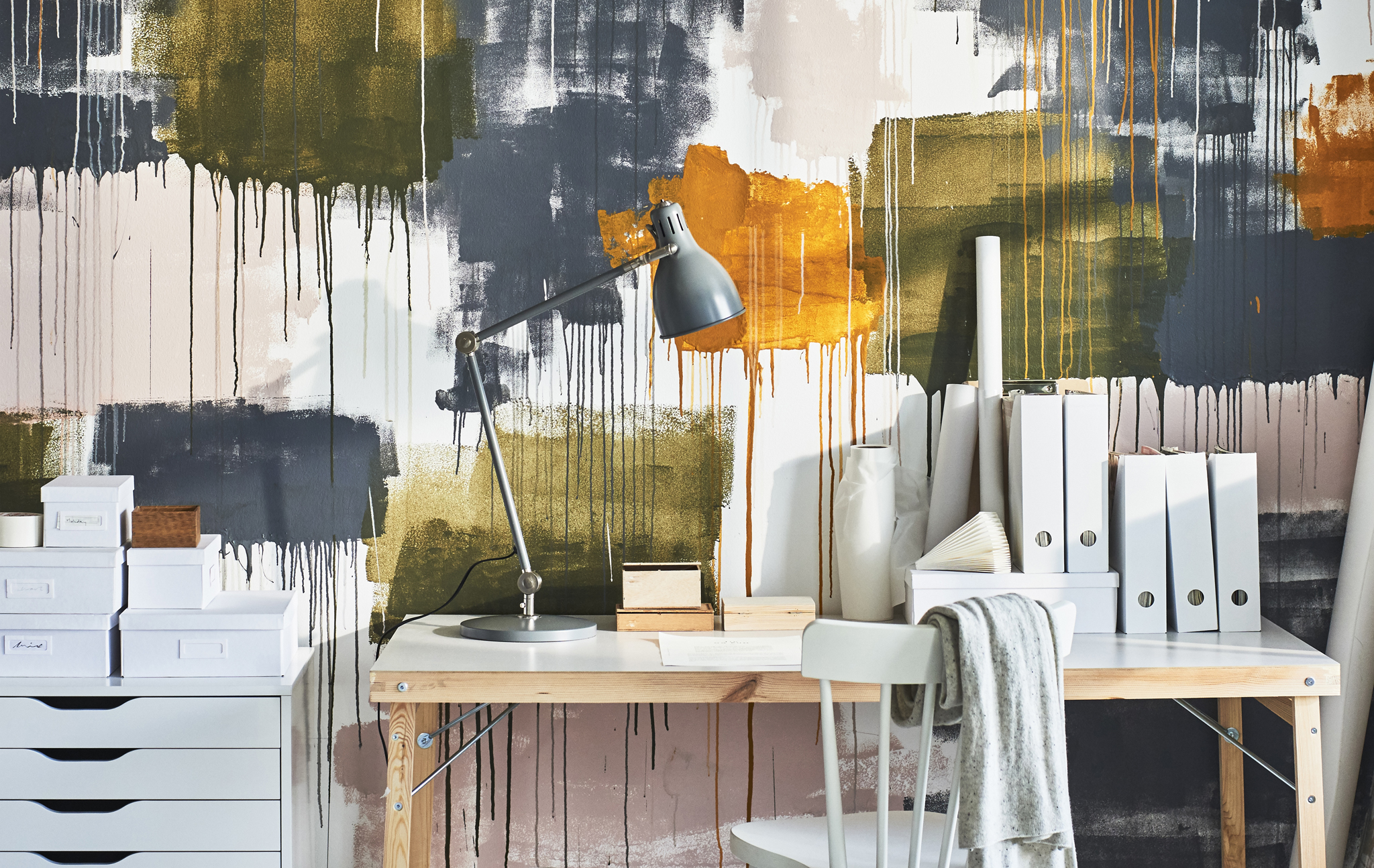 A desk, drawer and chair in a home office set against a wall decorated with big splatters of different coloured paint.