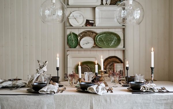 A dining table set for a festive meal with linen table cloth, candles, glassware and place settings with decorated napkins.