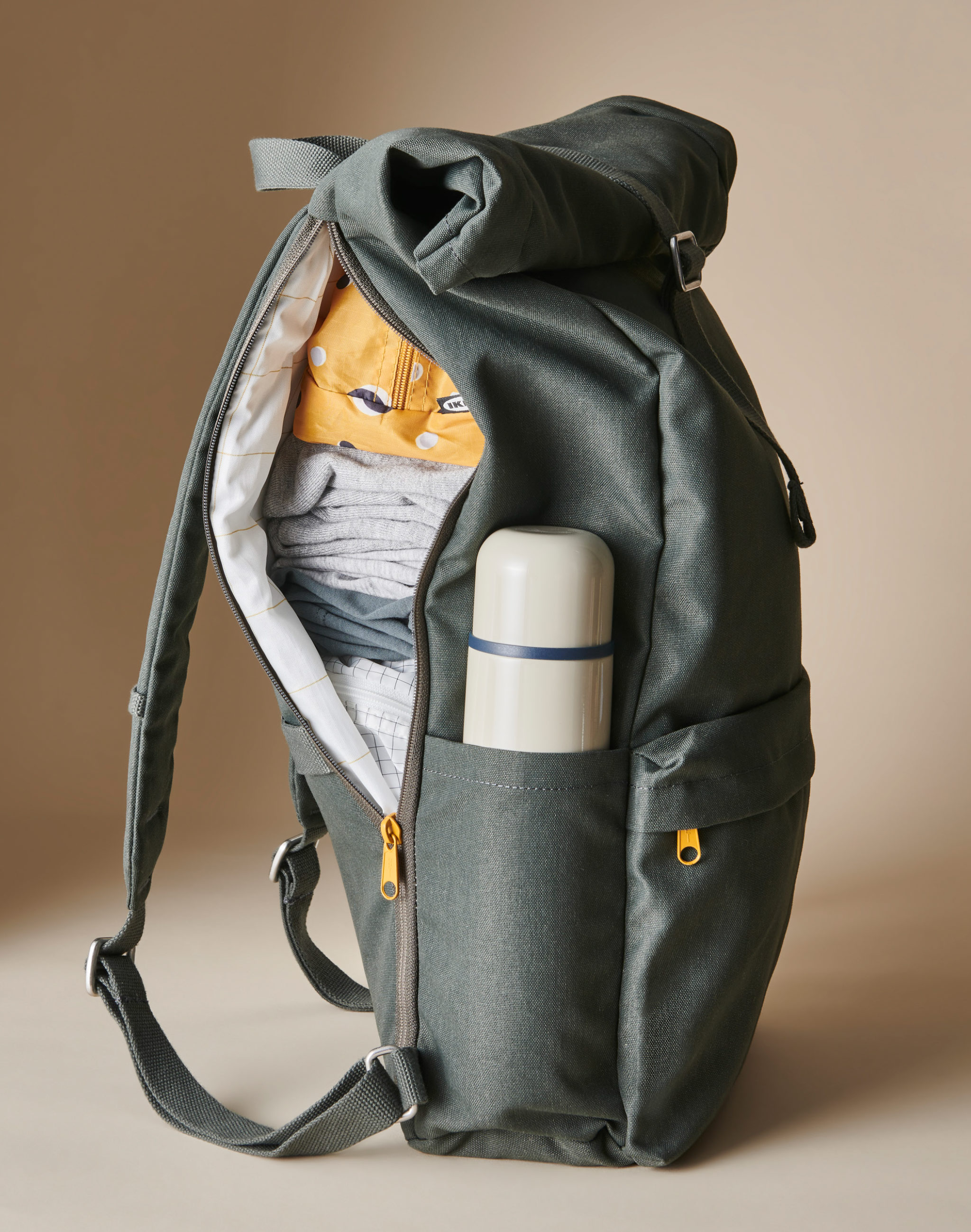 A green DRÖMSÄCK backpack unzipped on one side, filled with clothing, RENSARE bags, and a HÄLSA thermos.