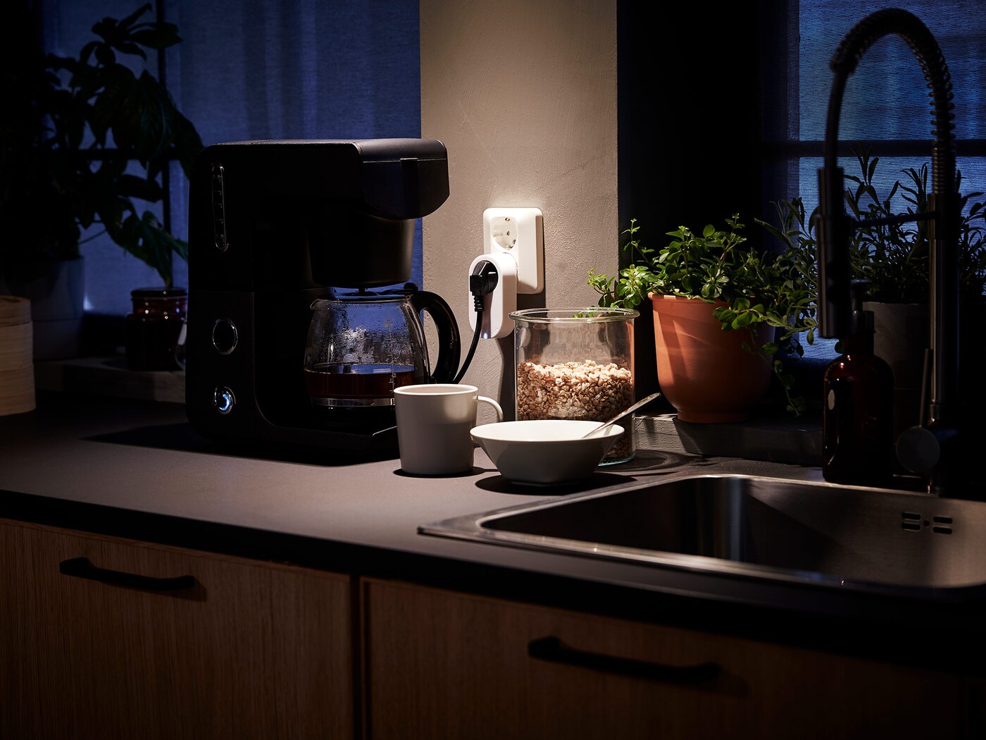 A kitchen work top with a coffee maker connected to an outlet control, and a cup and bowl beside a sink.