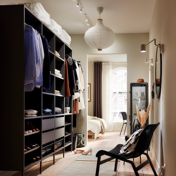 A large, open wardrobe solution in dark grey with folded clothes on shelves, hanging clothes on rails and four drawers.