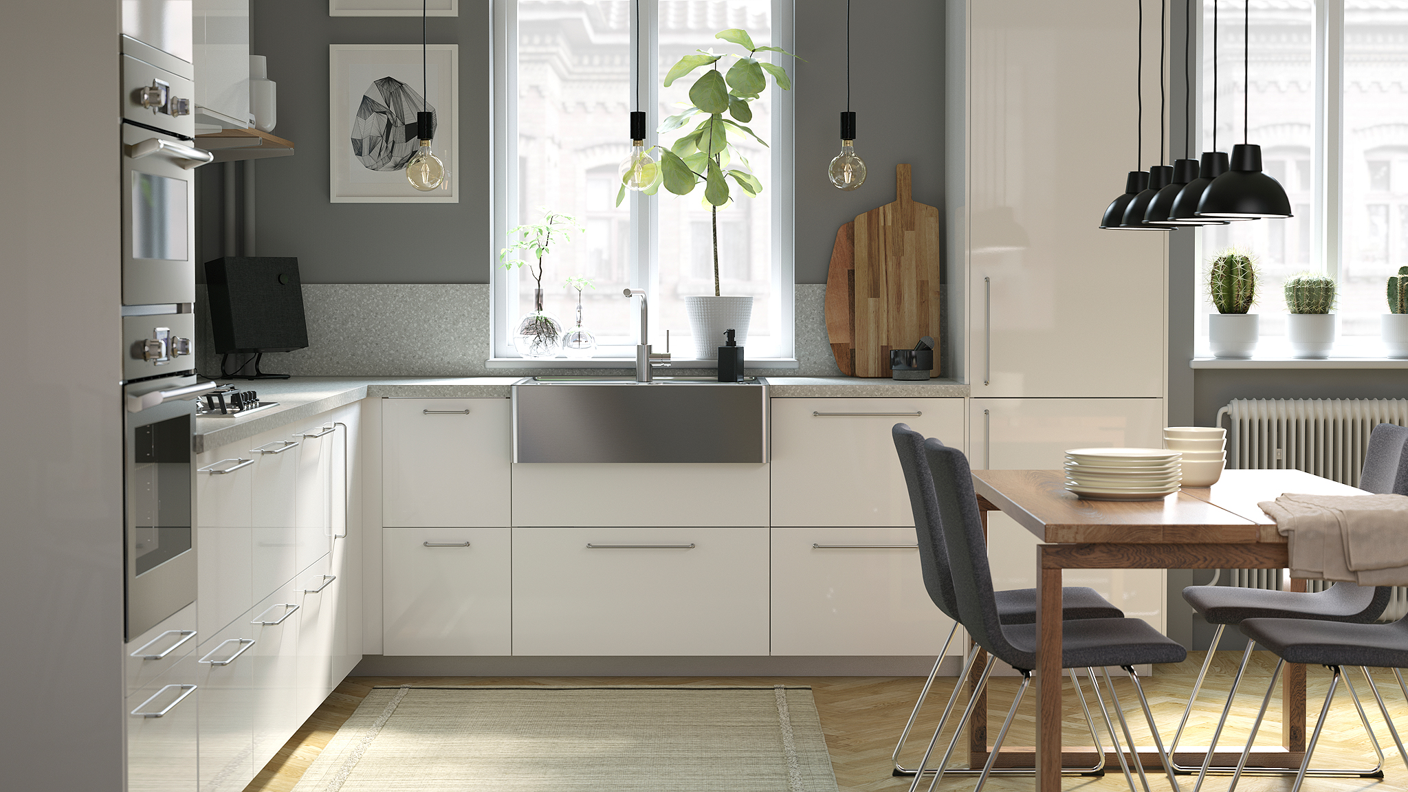 A light-filled kitchen with white shiny drawer fronts, grey walls, a wooden table, and a stainless steel sink.