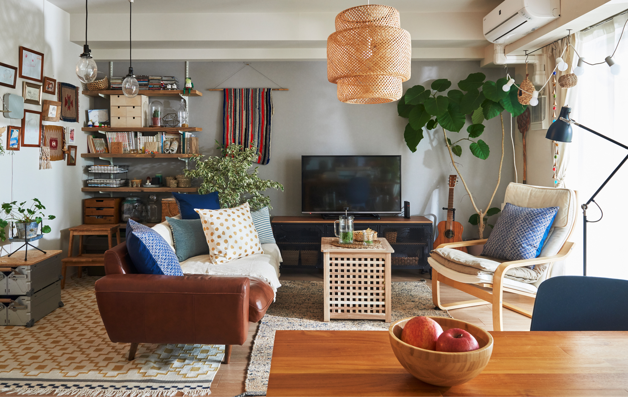 A living room with sofa, armchair, table, shelves and TV unit, and a large plant in the corner.