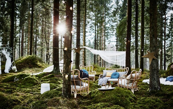 A lounge area in a forest wedding with rattan armchairs, lots of cushions and lighting chains next to a DIY photobooth