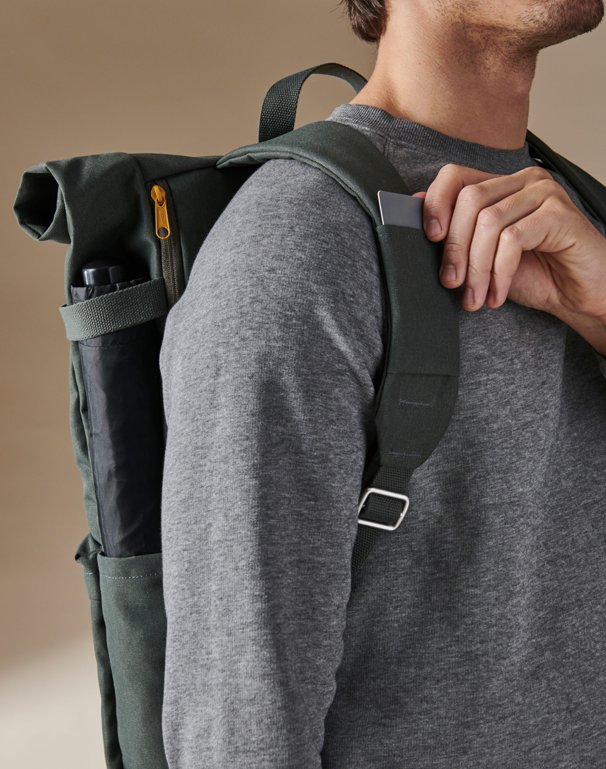 A man carrying a green DRÖMSÄCK backpack, taking out a card from the card slot on one of the shoulder straps.