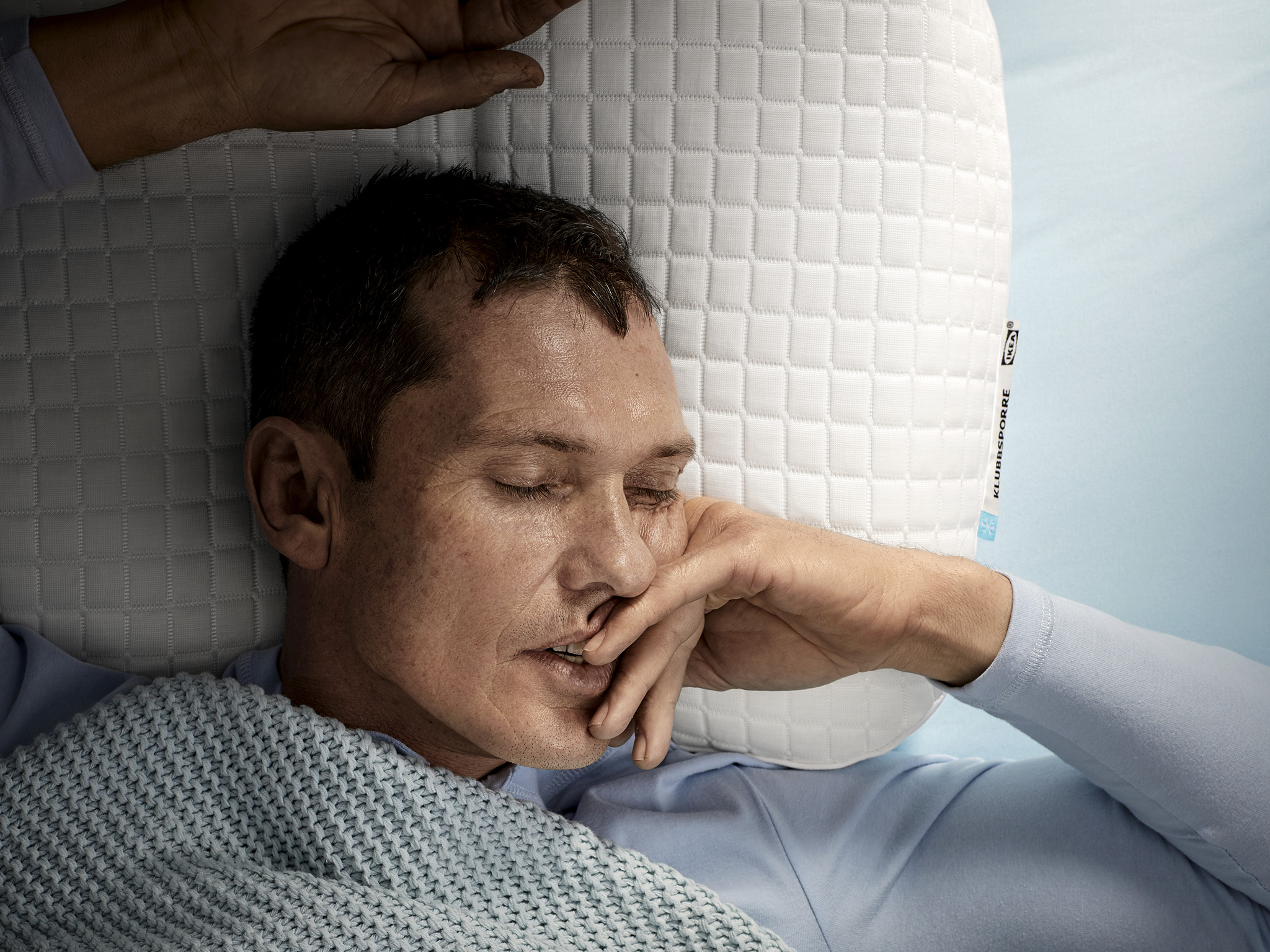 A man, laying on his back, is sleeping deeply on IKEA KLUBBSPORRE ergonomic pillow.