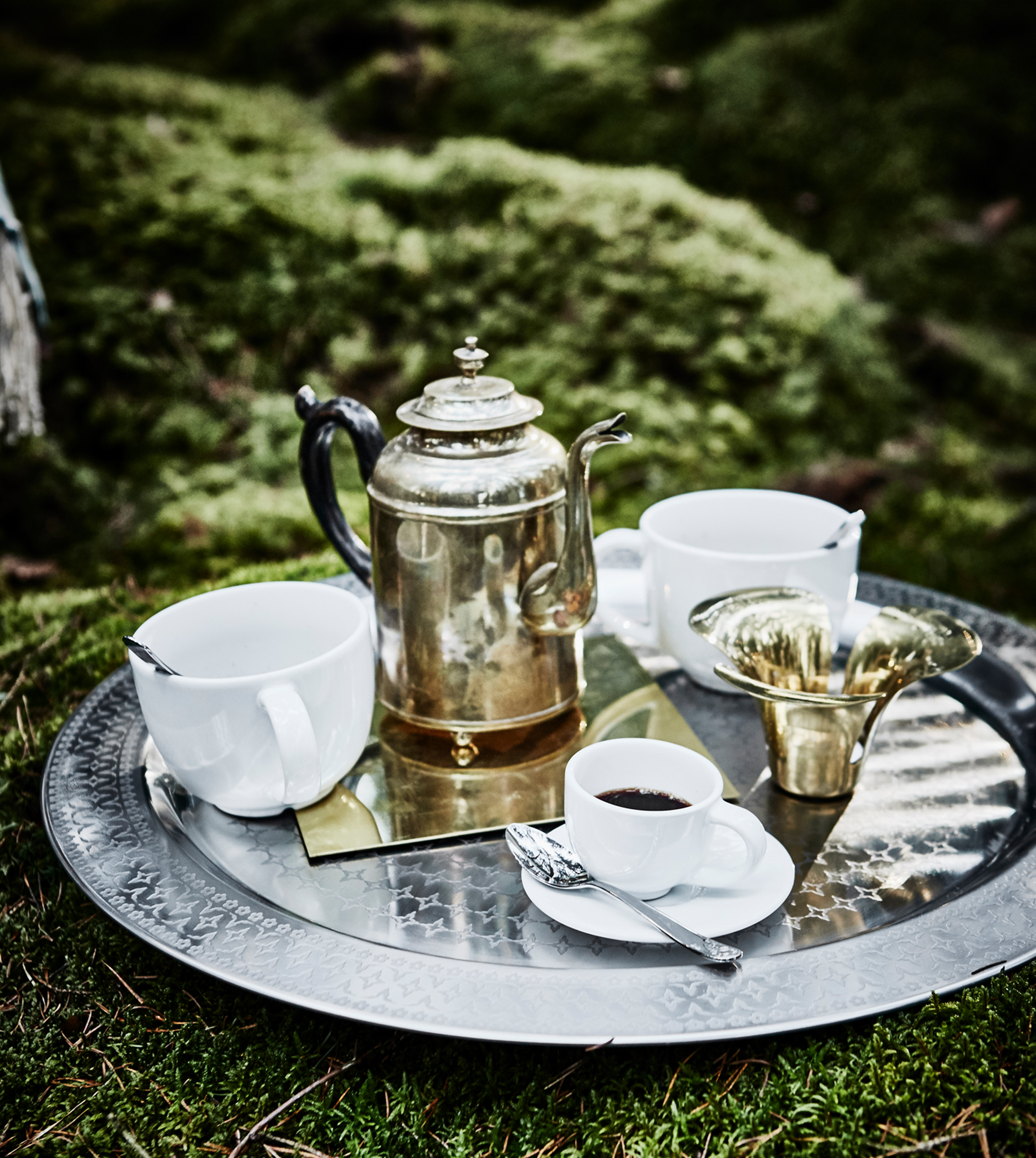A metal tray with cups of tea, coffee and a kettle resting on the ground in a forest wedding lounge