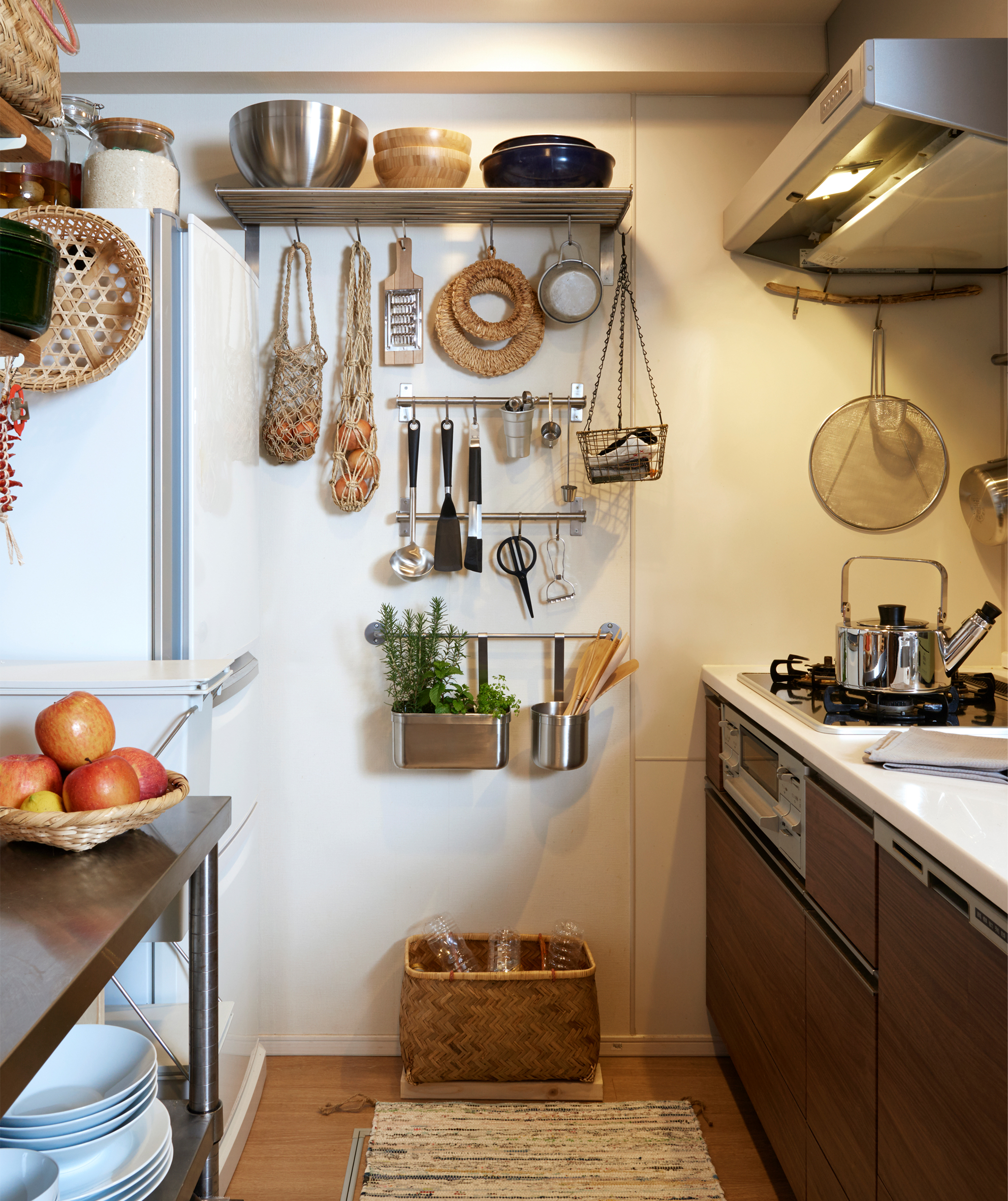A narrow kitchen with dark cabinets and utensils hanging on metal rails and shelves on the end wall.