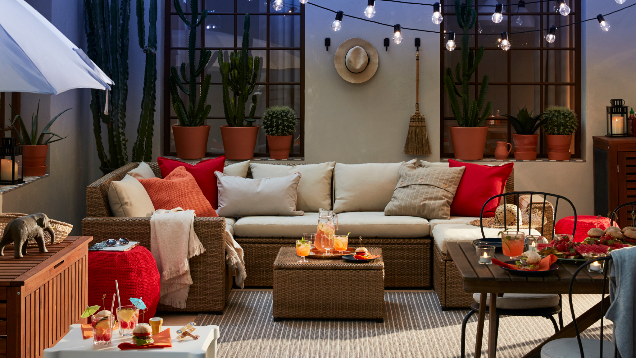 A patio with outdoor sofa and a smaller white table and stools, a dining table with chairs and a parasol.