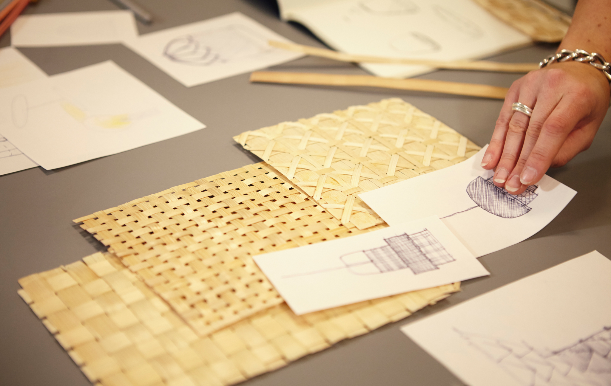 A person laying samples of woven bamboo and sketches out on a table.