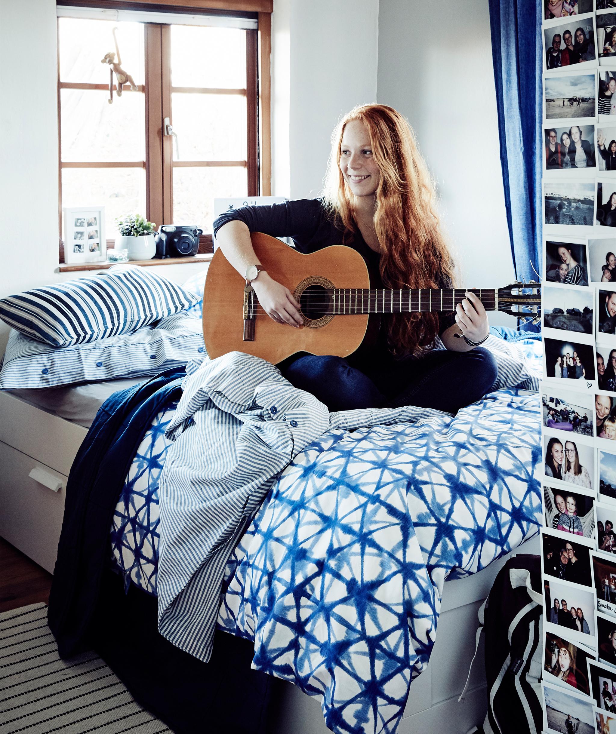A portrait of Stine playing the guitar on her bed.