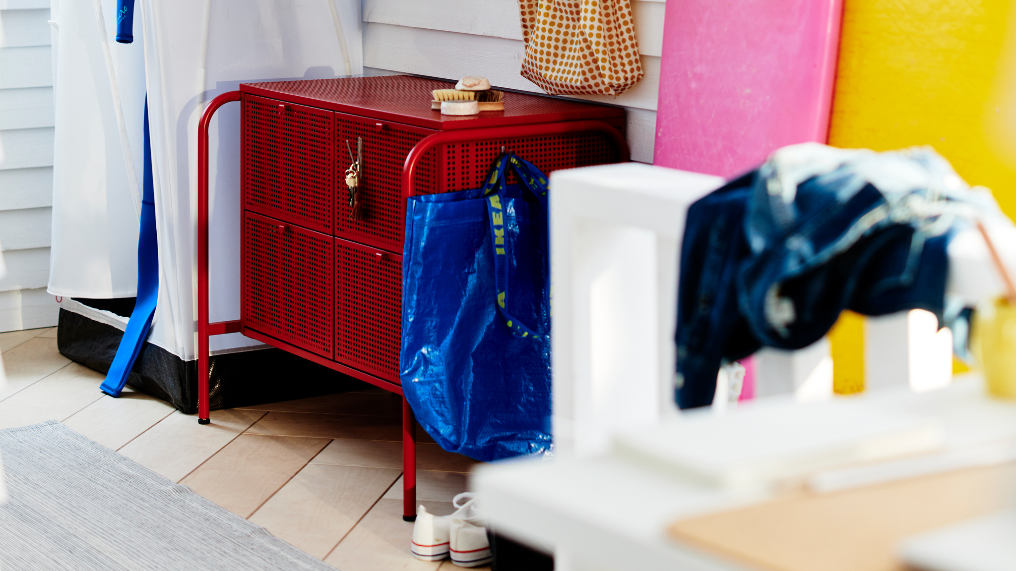 A red NIKKEBY chest of drawers surrounded by various hallway accessories in a clapboarded, white room.
