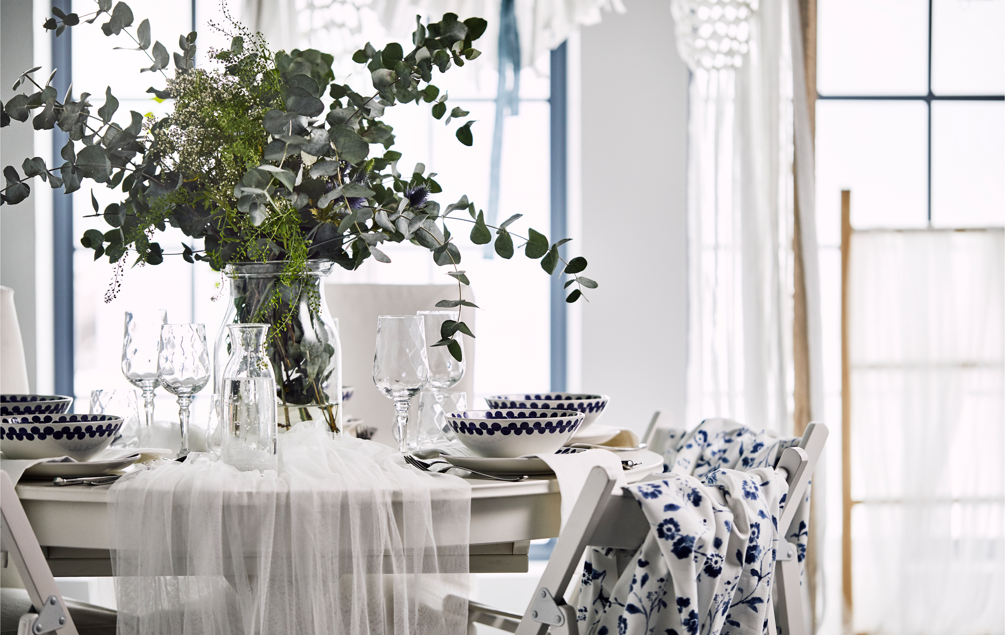 A romantic table setting with white tulle draped over a round table and a vase with wild flowers and eucalyptus leaves.