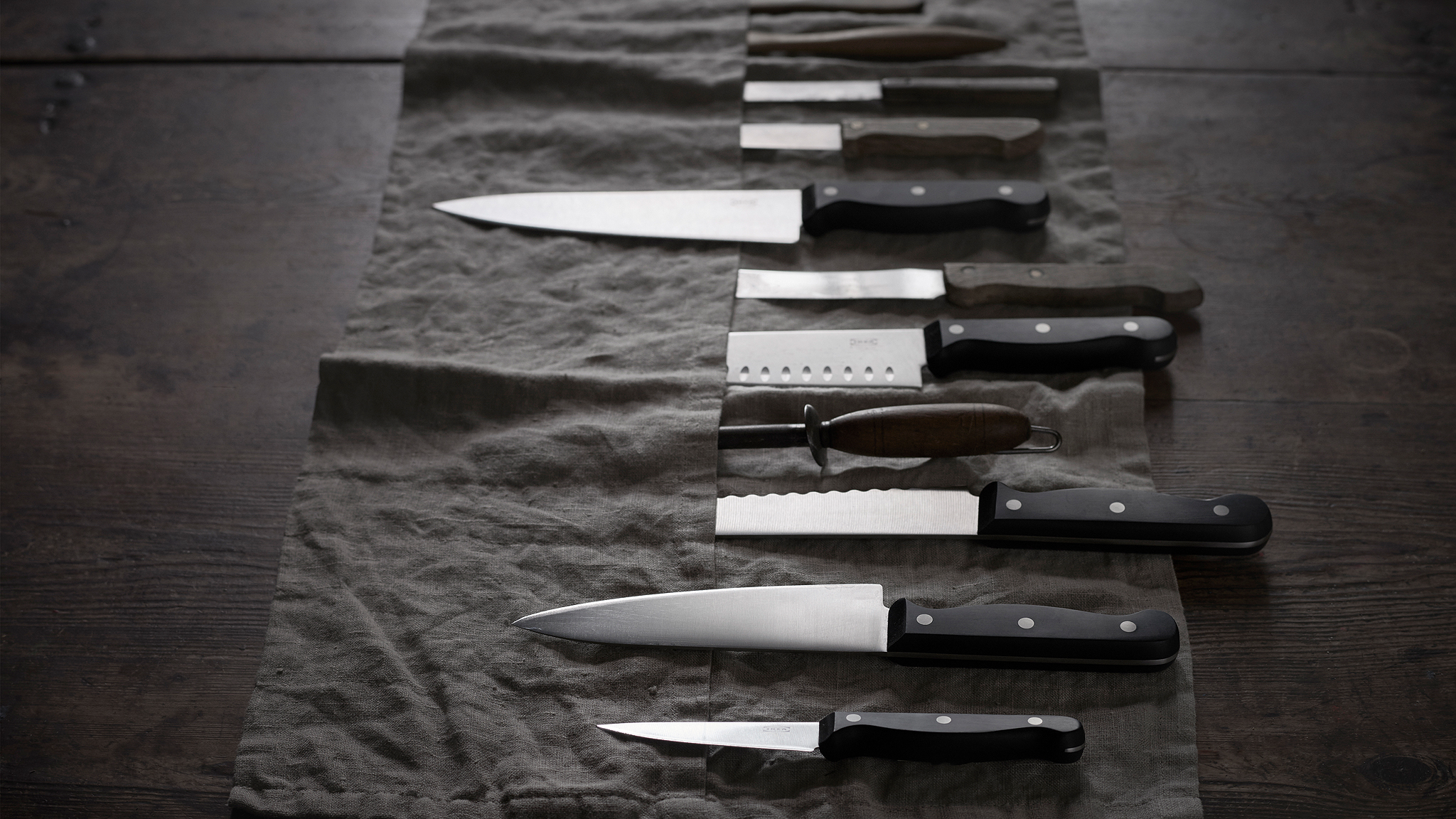A selection of VARDAGEN kitchen knives in various sizes laying on a dark-grey knife roll.