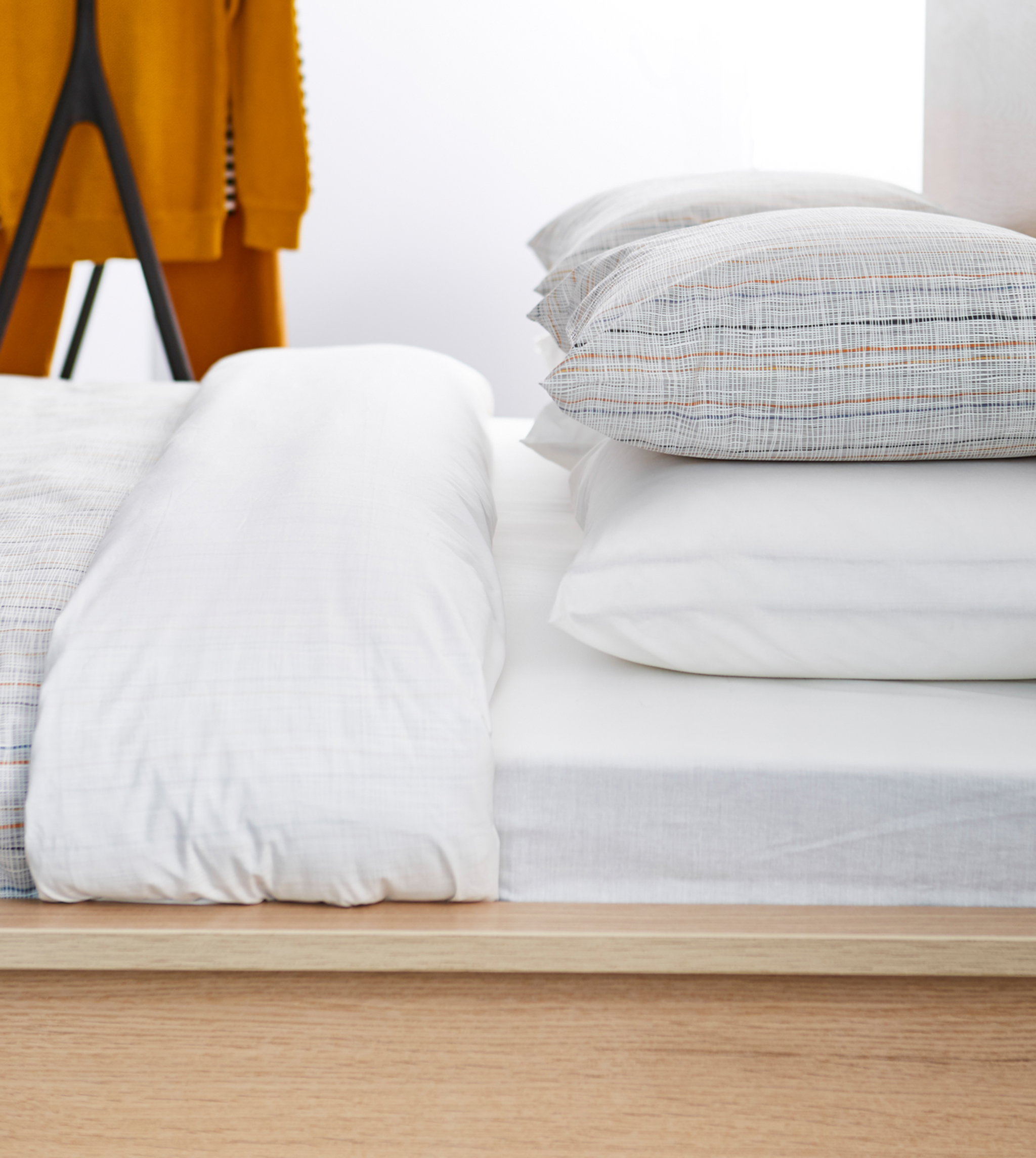 A sideview of a neatly made bed with white linens and simple striped pillows.