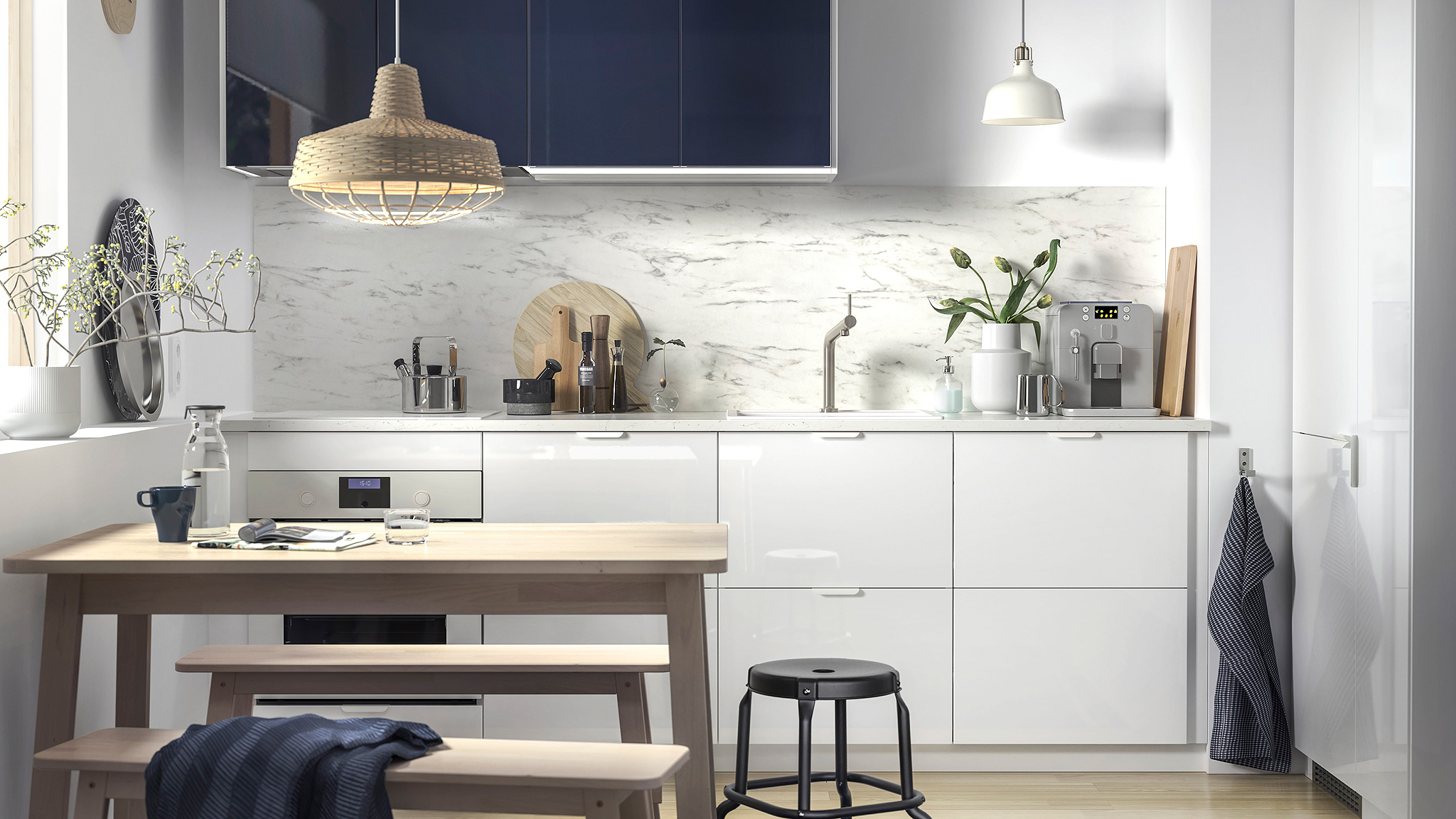 A small kitchen with white drawers and glossy black-blue kitchen cabinet fronts and a wooden table with two benches.